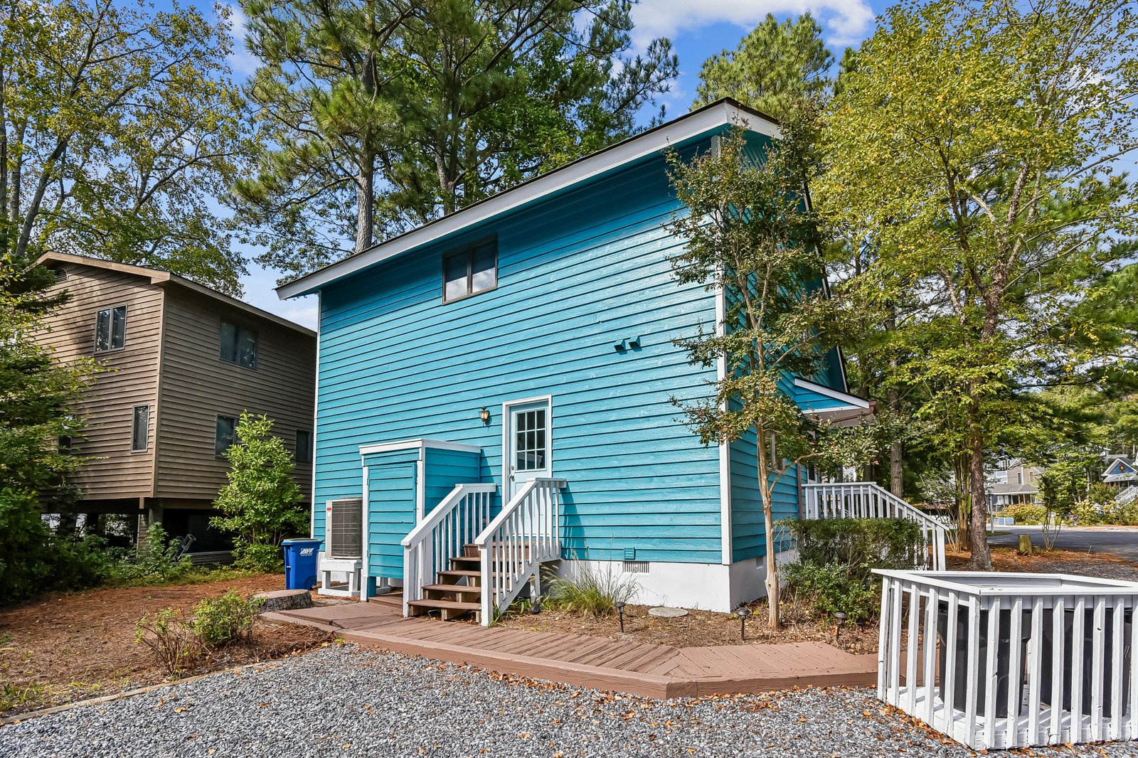 A cheerful turquoise exterior nestled among tall trees, offering a welcoming arrival in a peaceful, wooded neighborhood.