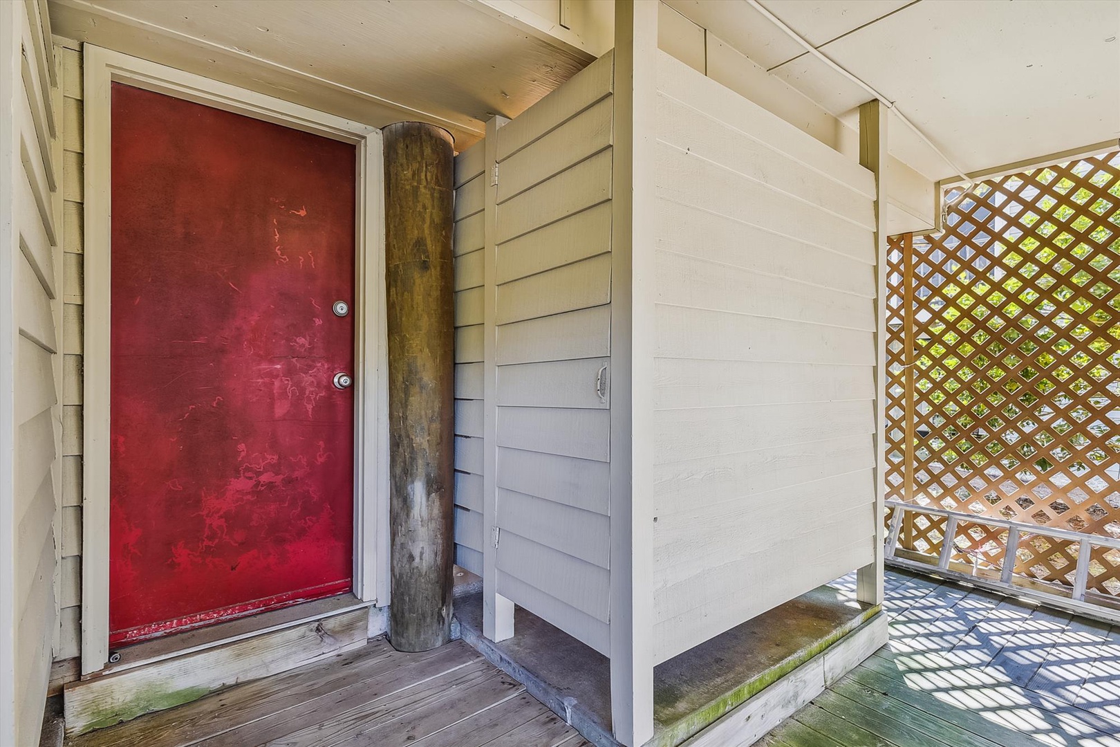Rustic entryway features a bold red door framed by natural wood beam, opening to a sunlit, latticed porch perfect for welcoming you to your retreat.