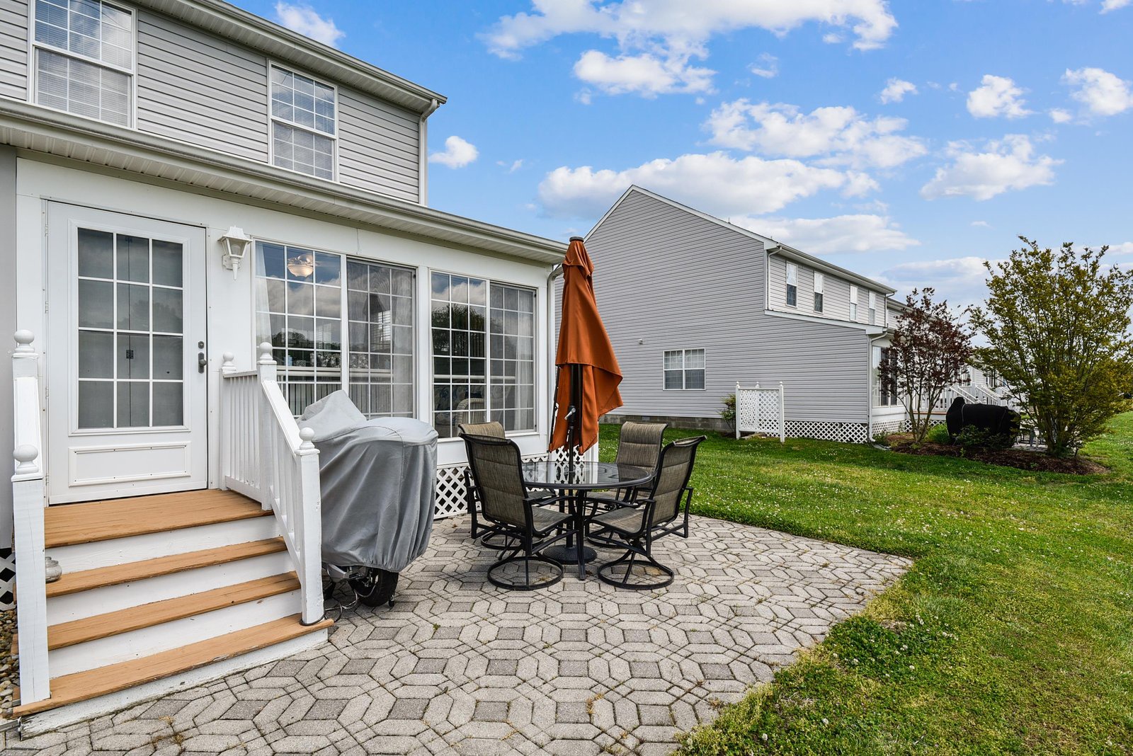 The property features a paved outdoor patio with dining furniture and an umbrella, adjacent to a spacious grassy backyard—ideal for relaxing or entertaining in a peaceful residential setting.
