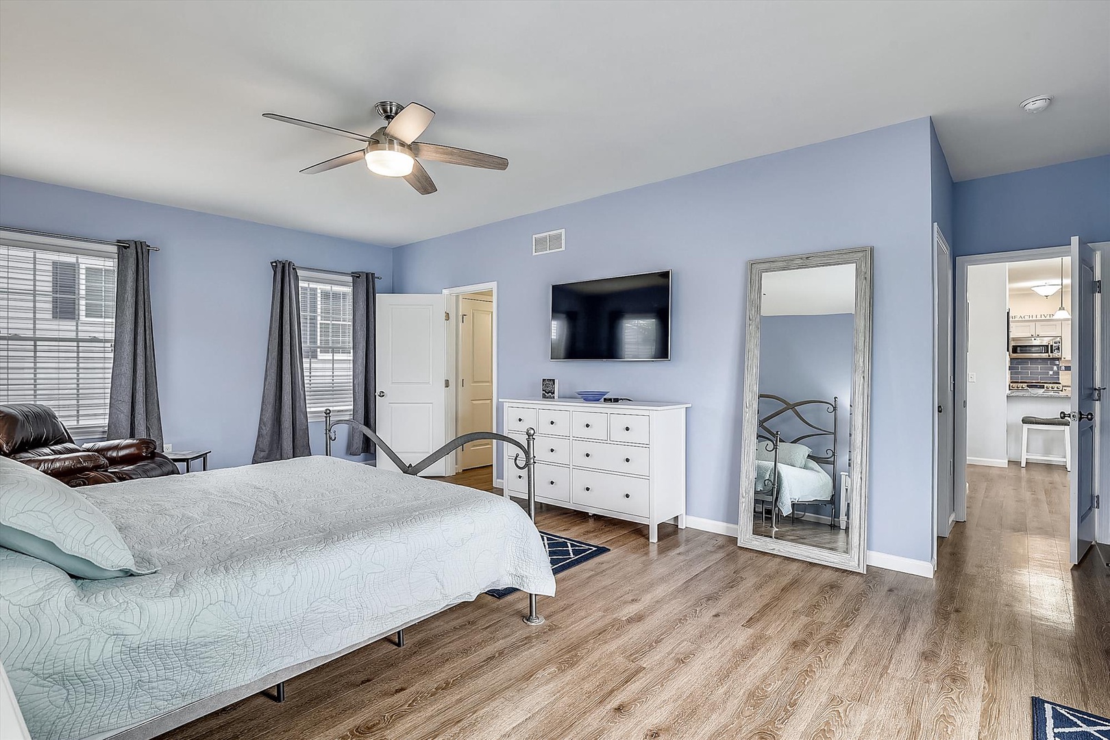Relax in your spacious bedroom with soothing blue walls, elegant hardwood floors, and ceiling fan keeping you comfortable. Large windows flood the room with natural light, while the TV and dresser add convenience to your stay.