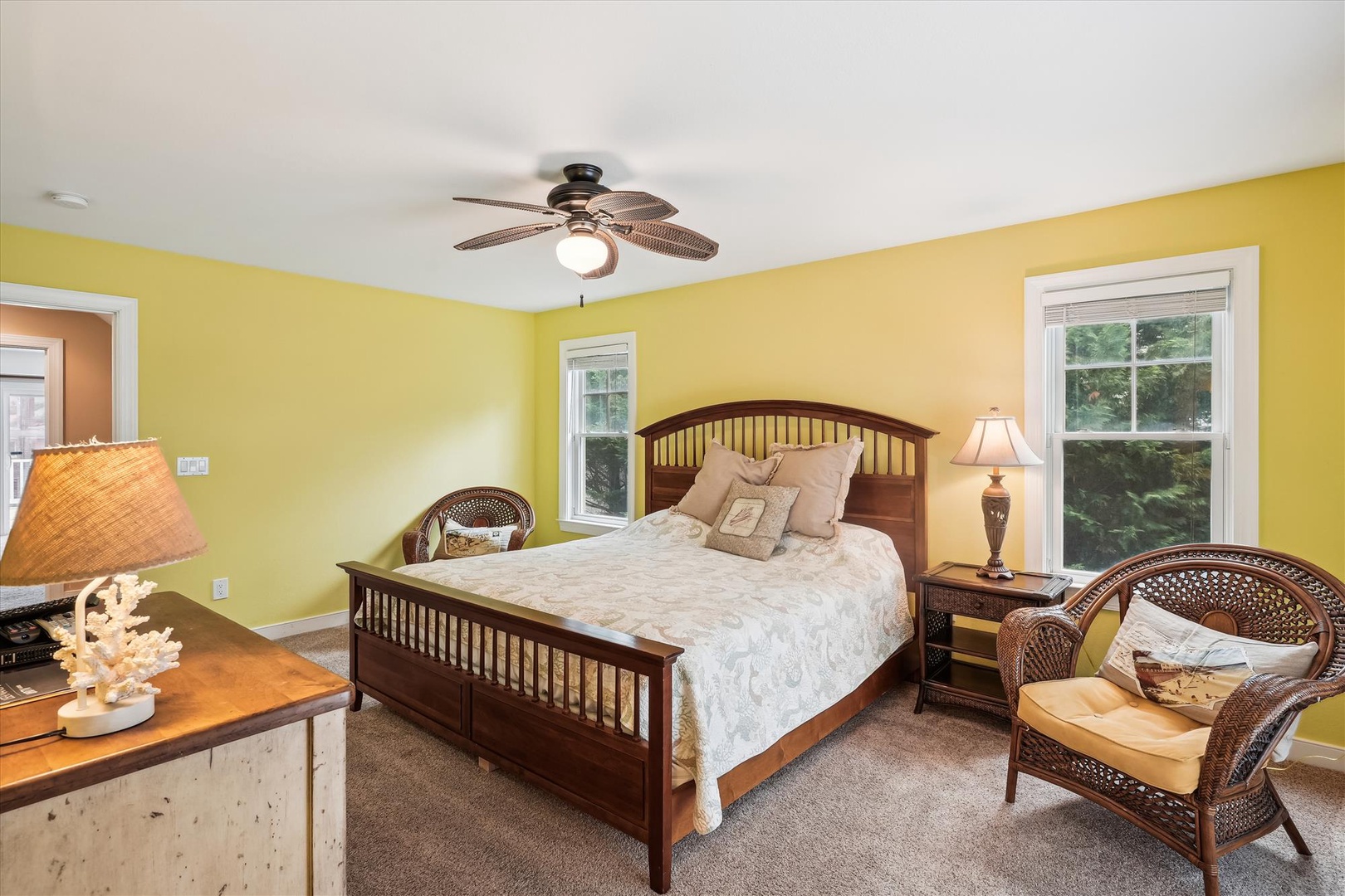 Sink into the soft bedding of this inviting bedroom, where cheerful yellow walls and natural light create a warm retreat. Relax in the wicker chair or enjoy the breeze from your private ceiling fan.