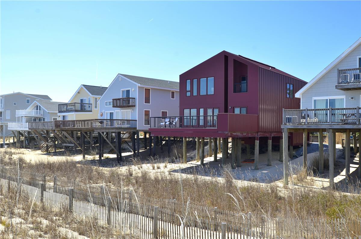 A collection of stilt homes stand along the beachfront, providing direct access to the sandy shore and the blue sky stretching across the horizon.