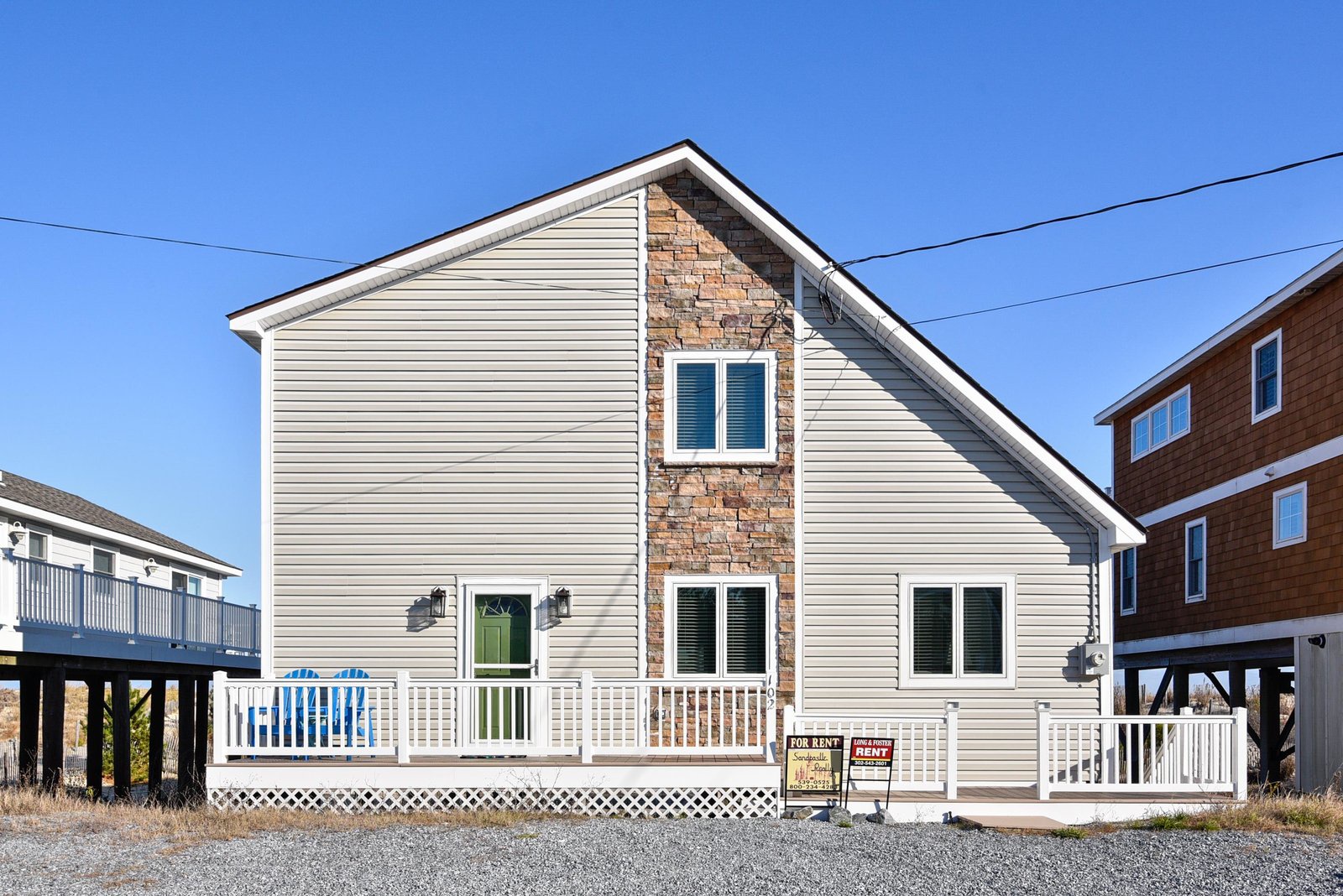This coastal property features a bright green front door, a distinctive stone-accented facade, and a wraparound deck perfect for enjoying the sea air.
