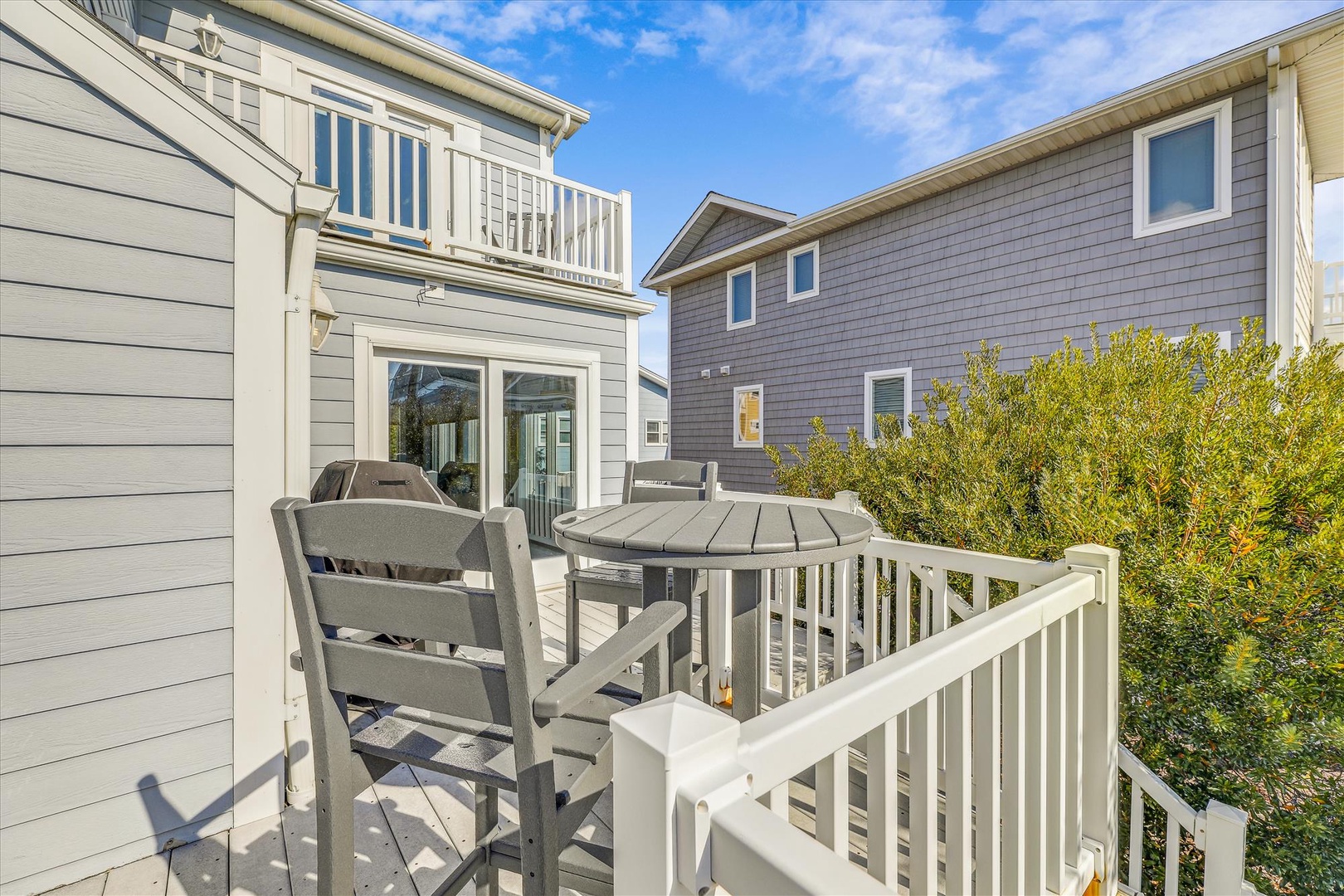 Private outdoor deck surrounded by greenery and neighboring homes, offering a sunny spot for morning coffee or relaxed meals al fresco in a peaceful residential setting.