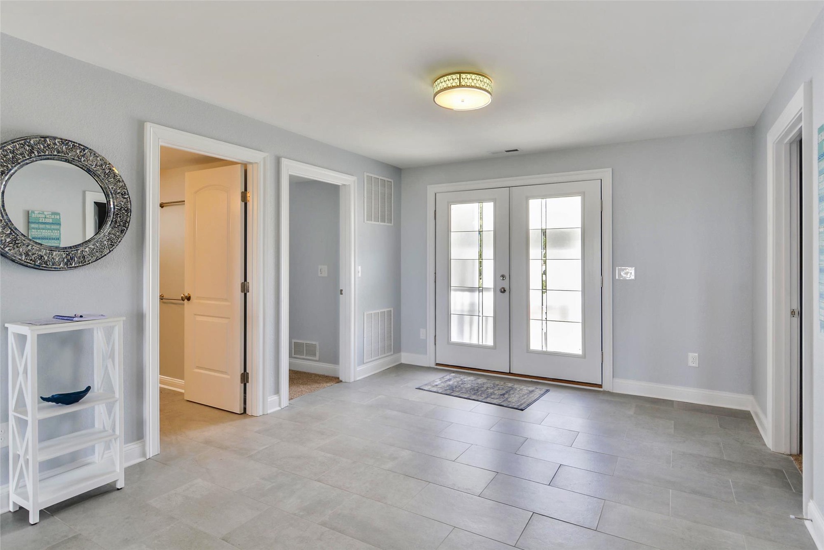 Step into a bright, welcoming entryway with stylish tile floors, soft gray walls, and glass-paneled French doors flooding the space with natural light—your perfect home base awaits.