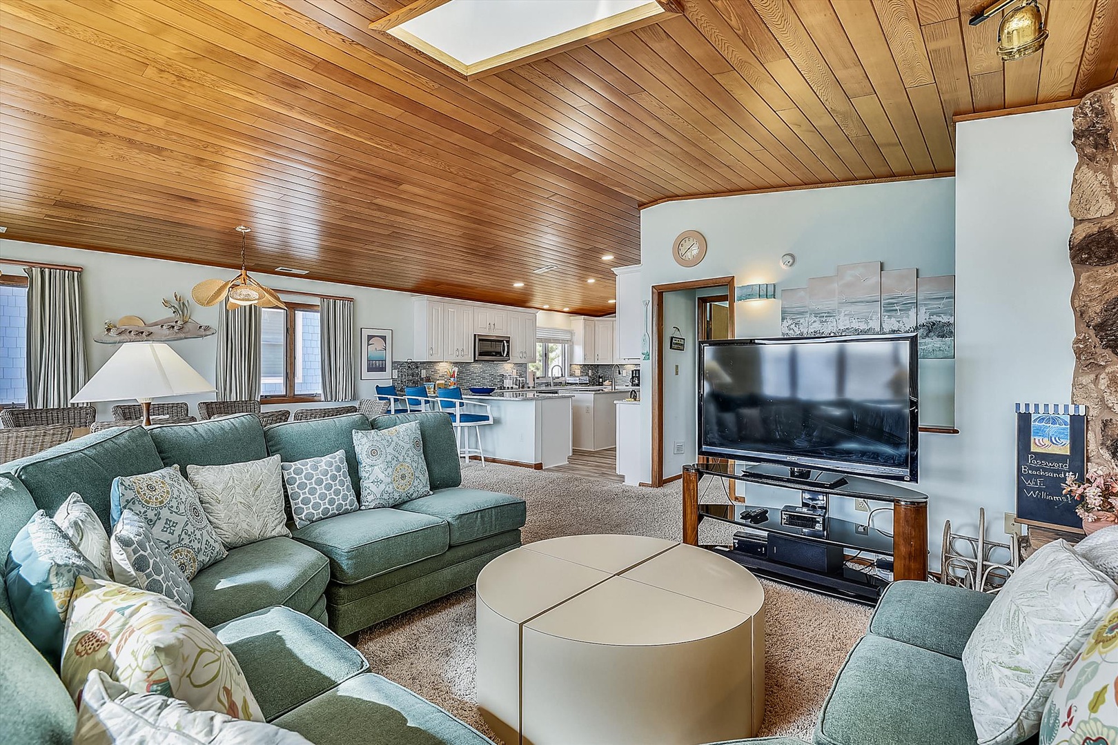 Cozy up in this inviting living room with plush seating, warm wood ceilings, and natural light from a skylight. Your perfect mountain retreat awaits, seamlessly connecting to a well-equipped kitchen for your convenience.