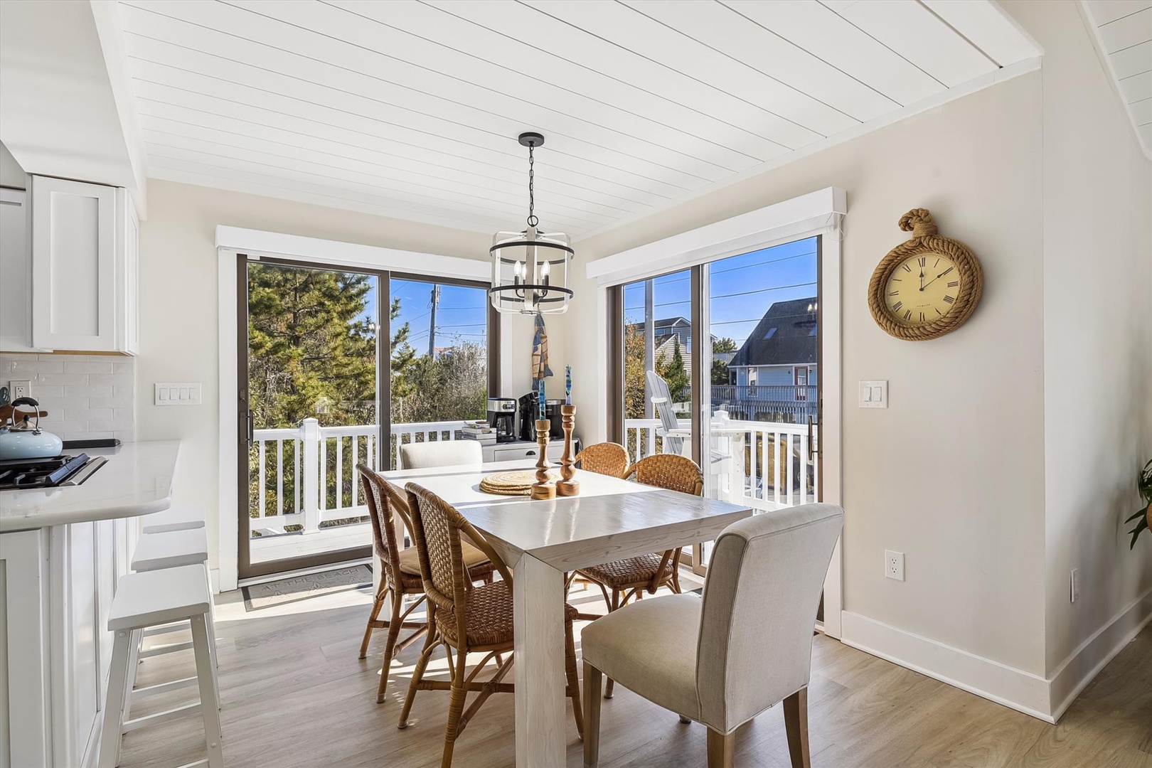 Gather around this bright dining table where sunlight pours through tall windows, inviting you to enjoy meals with views of the coastal neighborhood and refreshing ocean breeze.