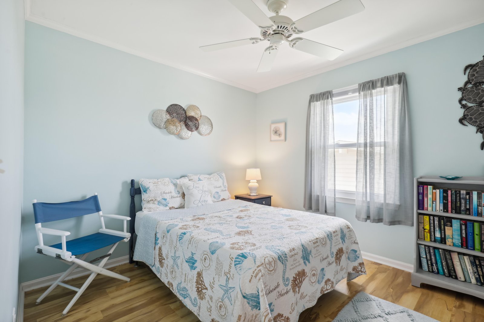 Relax in your serene coastal-inspired bedroom, where soft blue tones and breezy ceiling fan create a peaceful retreat. Curl up with a favorite book or drift off to the soothing seaside ambiance.