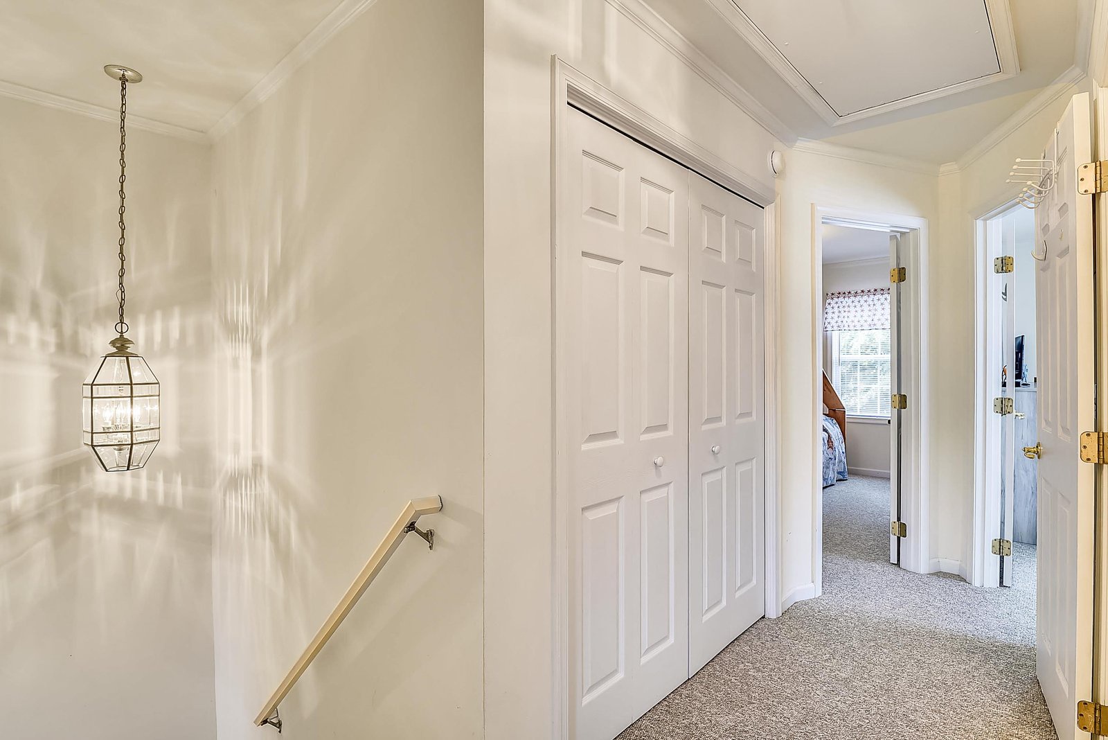 Soft natural light filters through this charming hallway, where a coastal-inspired lantern creates gentle patterns on your walls and plush carpeting leads toward inviting bedrooms.