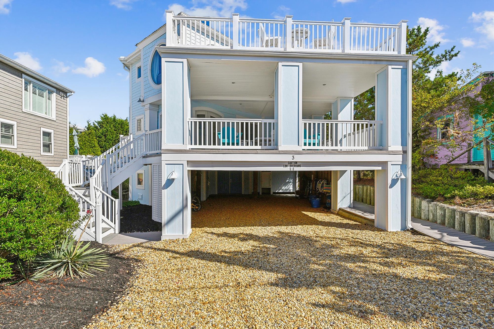 Coastal vacation home featuring covered parking, multiple balconies, and a rooftop deck, set in a quiet residential neighborhood near the beach.