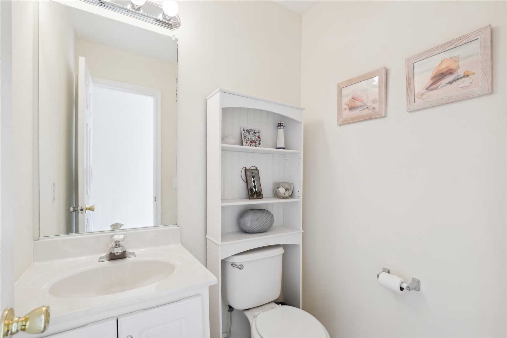 Your private bathroom features a clean vanity with mirror, fresh towels, and thoughtful shelving for your essentials. Coastal-inspired art adds a serene touch to this peaceful retreat.