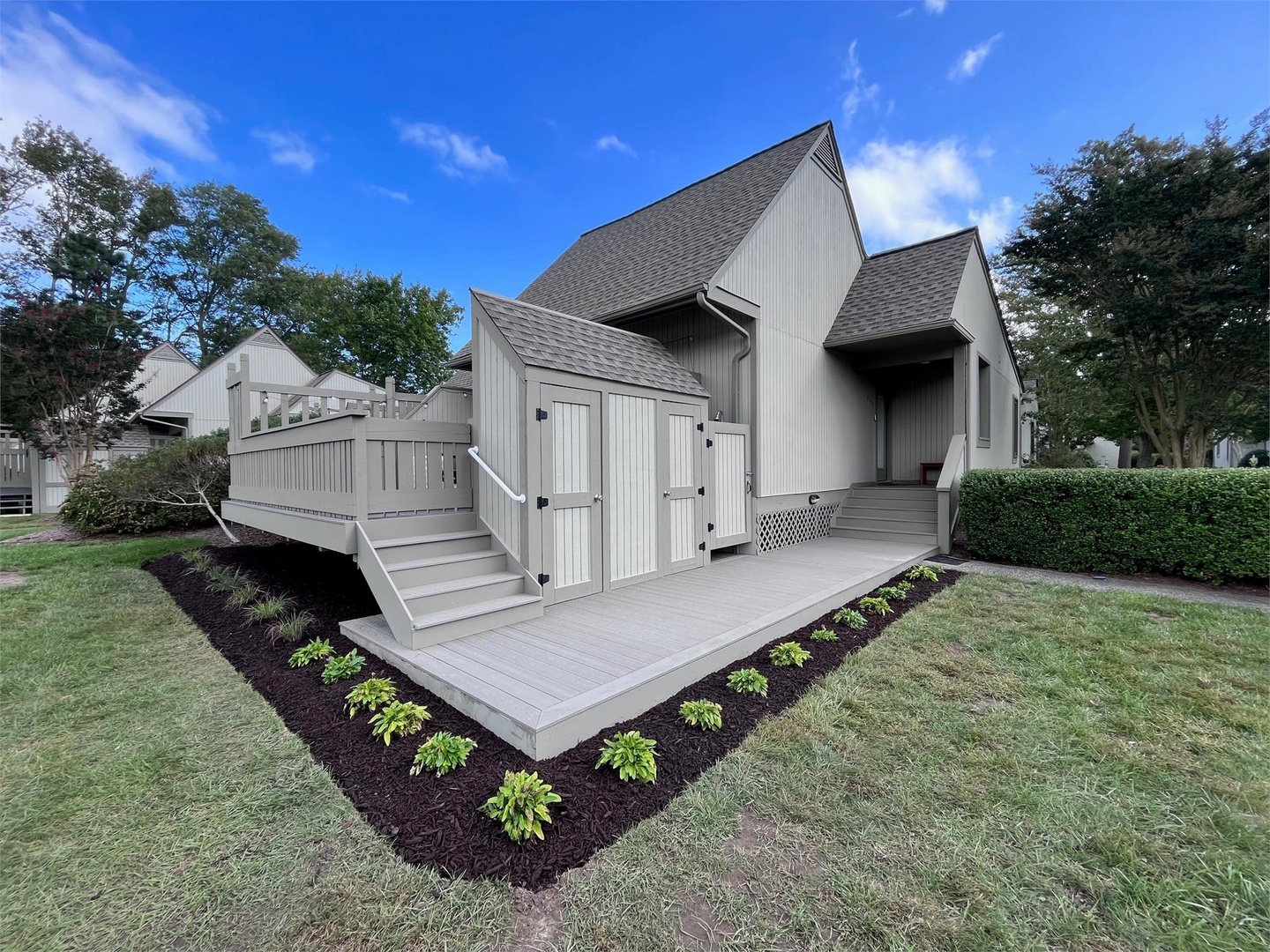 Modern coastal home with bright vertical siding, accessible ramps, and manicured landscaping nestled in a peaceful residential community under blue skies.