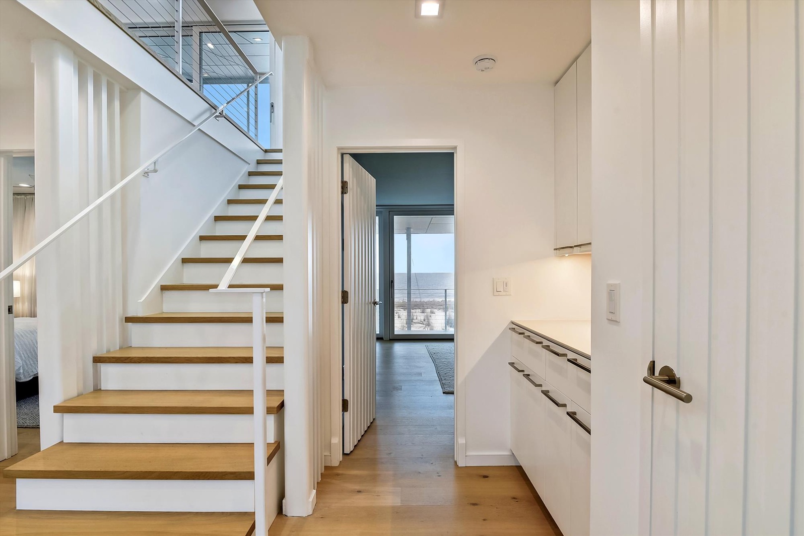 Modern, airy home with warm wood stairs and sleek white design connecting your space to a peaceful ocean vista beyond.