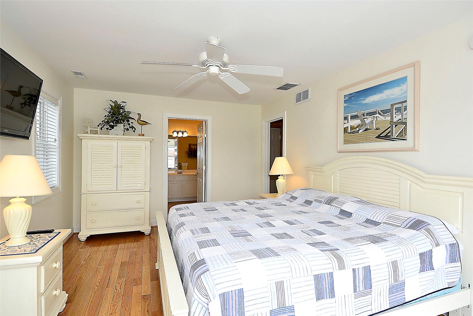 Drift off in your coastal-inspired bedroom with hardwood floors, a ceiling fan, and charming beachside artwork that captures the relaxed vibe of your vacation retreat.