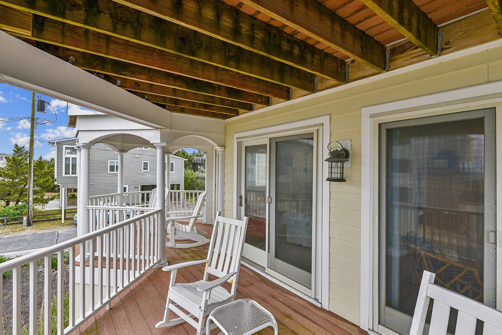 Settle into your rocking chair on this covered balcony and enjoy the coastal breeze. The exposed wooden beams overhead add charm while neighboring homes peek through the trees beyond.