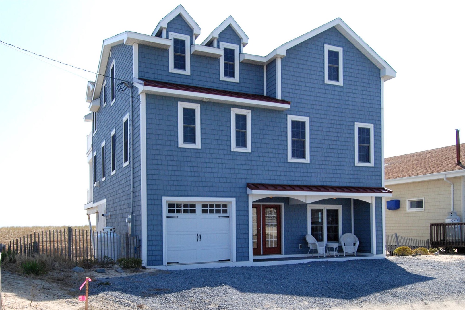 Coastal-style blue beach house with distinctive gabled dormers, steps from the sandy shoreline and dunes.