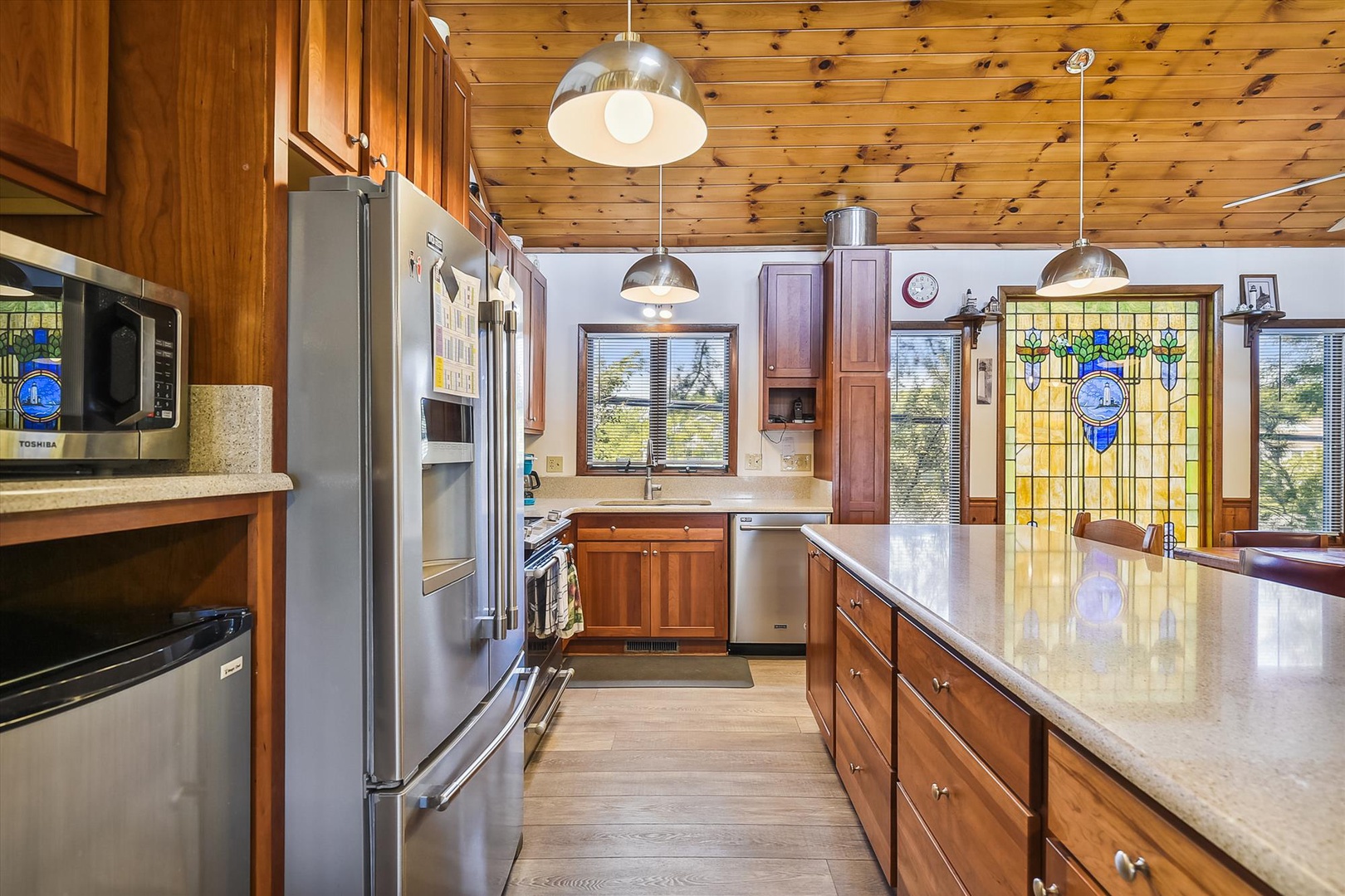 Cook your favorite meals in this warm, inviting kitchen featuring rich wood cabinetry, modern stainless steel appliances, gleaming countertops, and a charming stained-glass window—perfect for gathering, cooking, and creating memories during your stay.