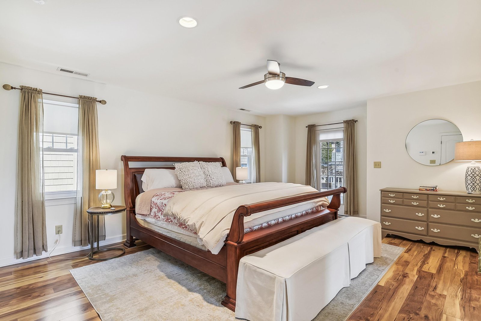 Sink into crisp linens under a gently whirring ceiling fan in your spacious retreat, where morning light spills through three windows and polished hardwood floors add warmth underfoot.