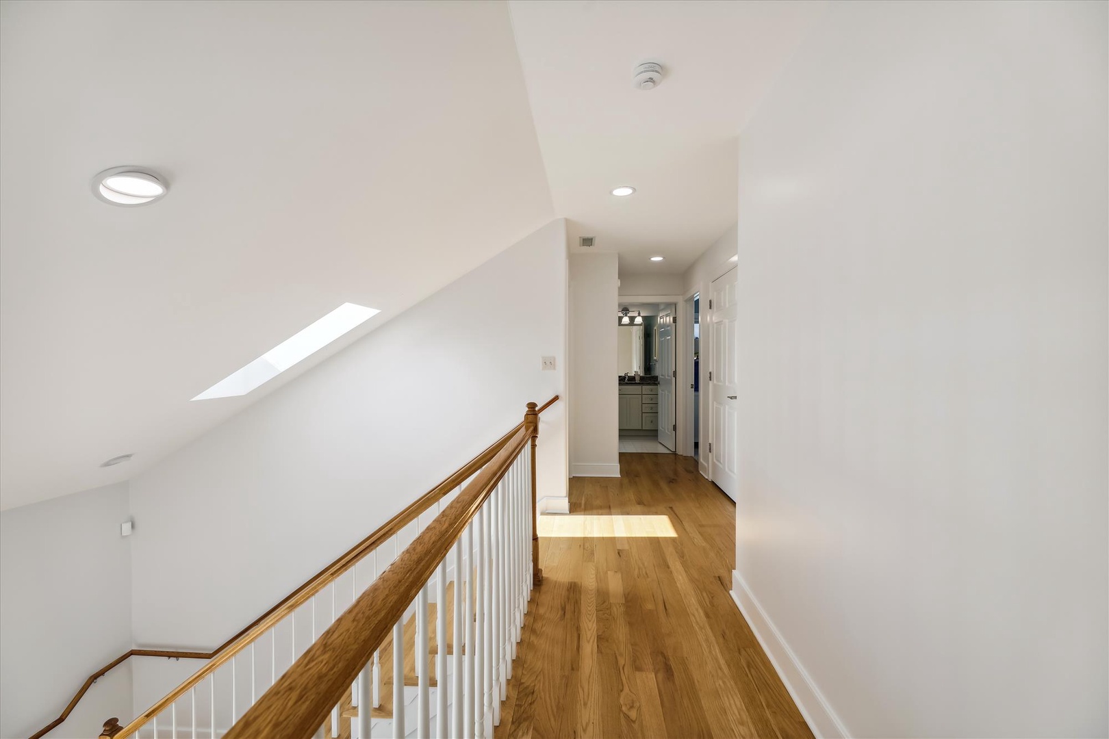 Warm natural light fills your upstairs hallway, where gleaming hardwood floors guide you past thoughtfully designed spaces bathed in soft brightness.