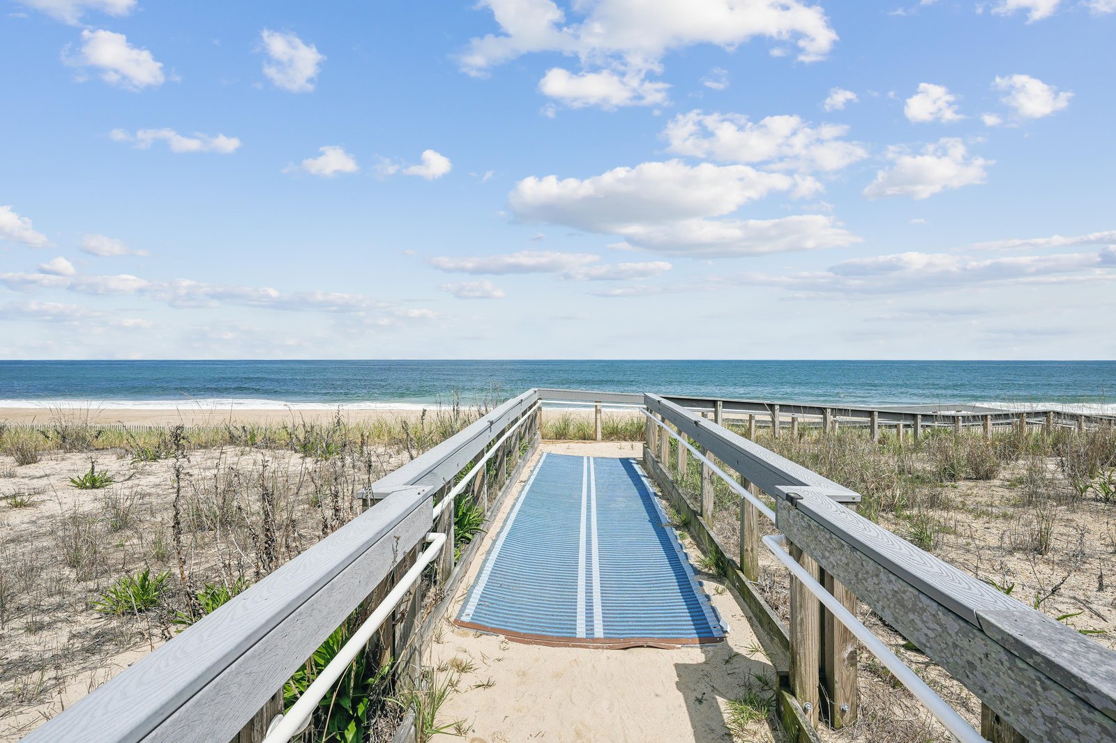 An accessible boardwalk leading to sandy shores and inviting ocean waves, where coastal dunes meet pristine beachfront under open skies.
