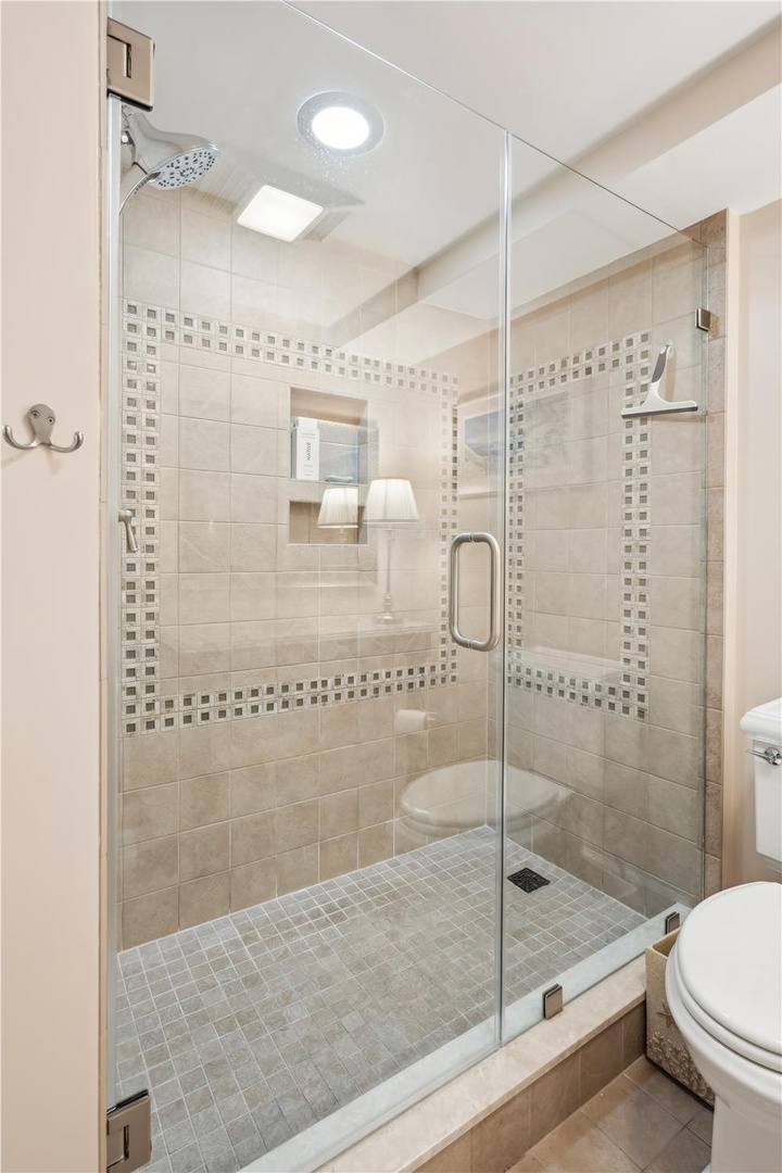 The spacious walk-in shower features elegant tile work with decorative accents, a rainfall showerhead, and a glass enclosure that fills the space with natural light.