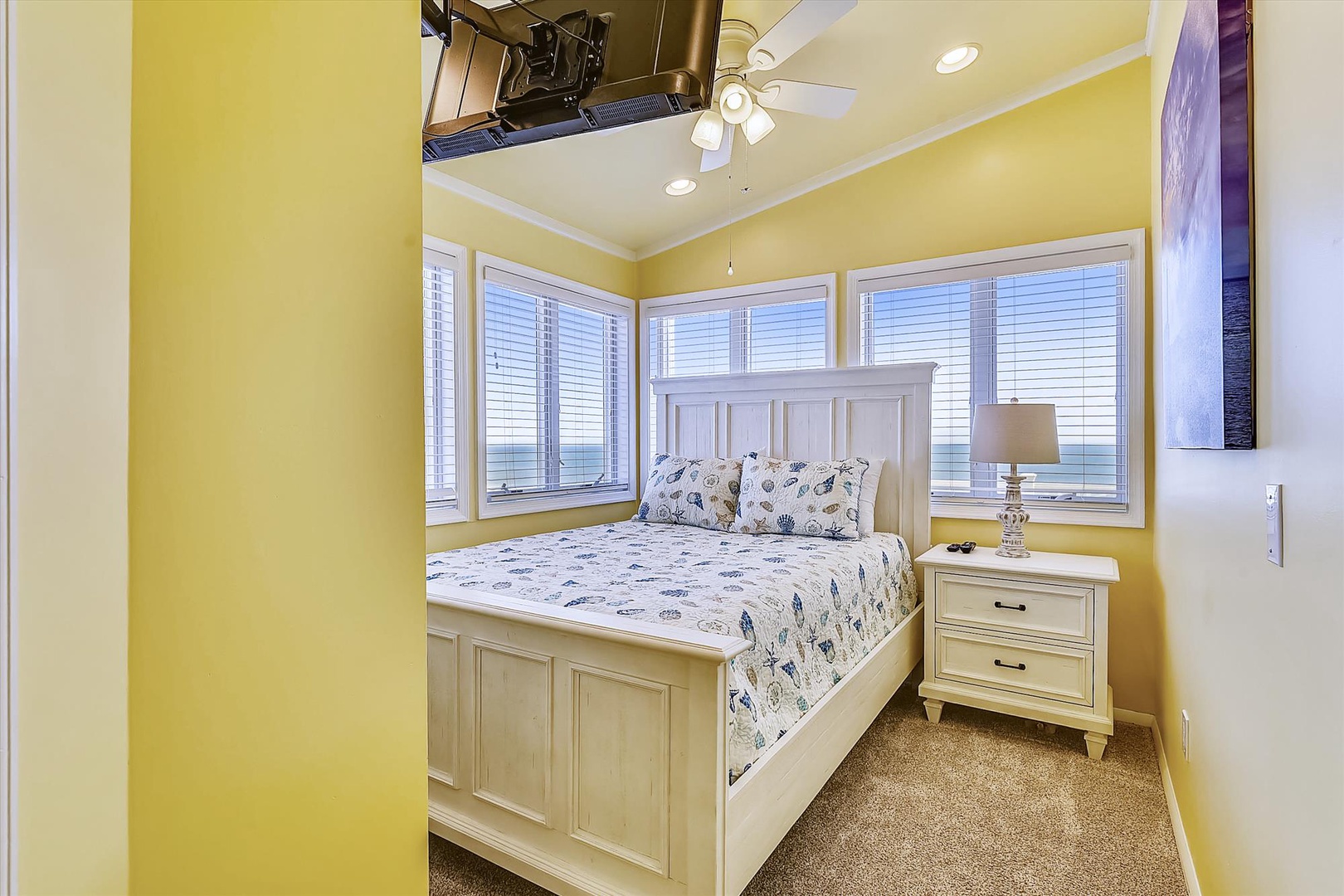 Drift off to sleep in your cheerful coastal bedroom with a comfy queen bed, ceiling fan, and peaceful sea views framed by three bright windows.