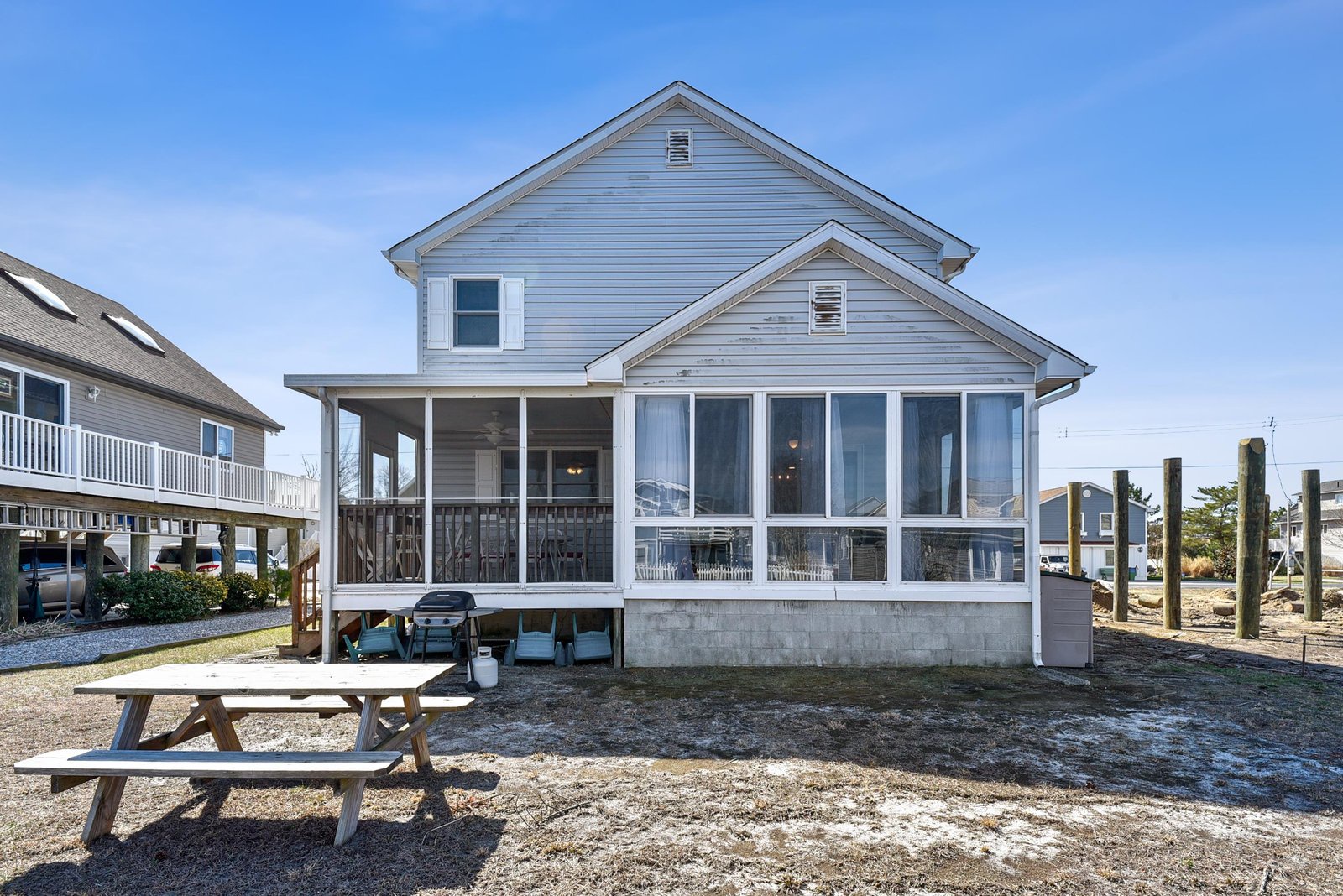 Coastal vacation home featuring a welcoming screened porch with a picnic table in the backyard, perfect for outdoor gatherings and relaxation.