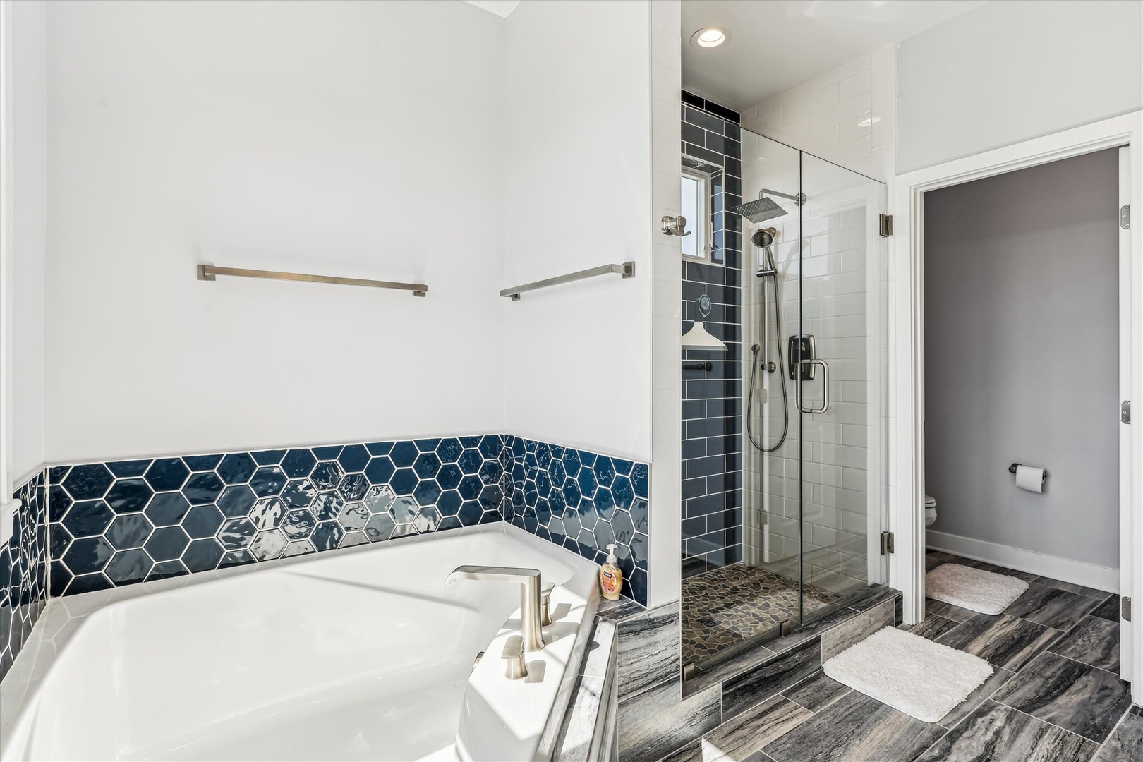 Unwind in your spa-inspired bathroom featuring a soaking tub with elegant navy hexagon tile, a spacious walk-in shower, and stylish modern finishes throughout.