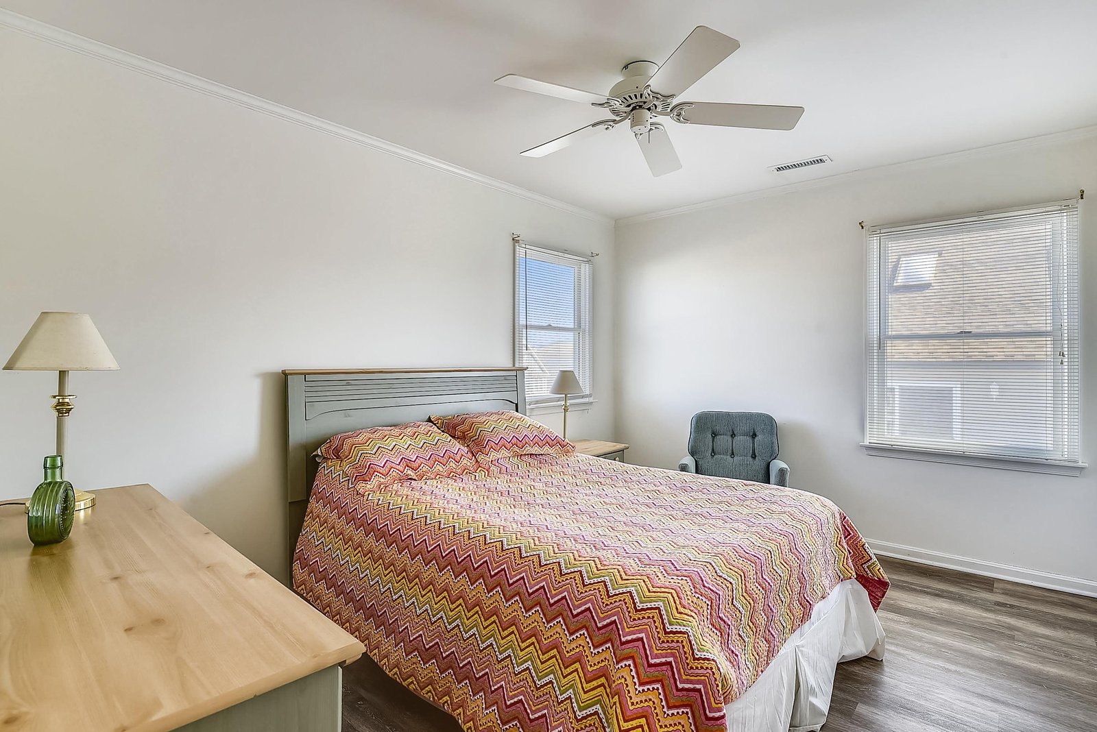 Your serene bedroom features a plush bed with cheerful linens, ceiling fan for comfort, and natural light streaming through dual windows to brighten your mornings.