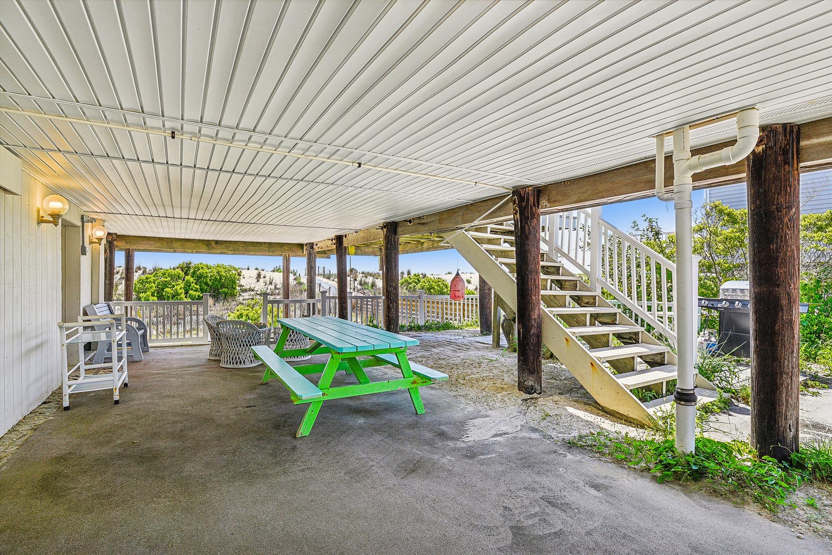 A shaded lower-level gathering area with picnic table, seating, and stairs leading upward, surrounded by greenery and coastal views.