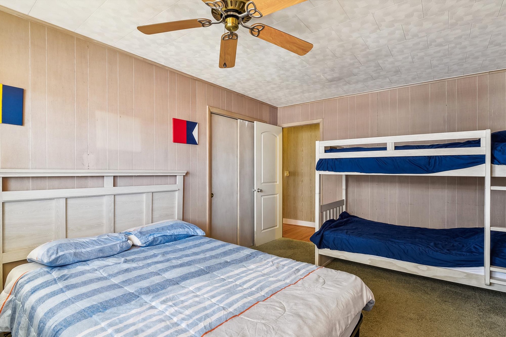 Relax in this cozy bedroom featuring a comfortable queen bed and bunk beds—perfect for families or groups. Nautical decor and a ceiling fan create a breezy, beachy vibe.
