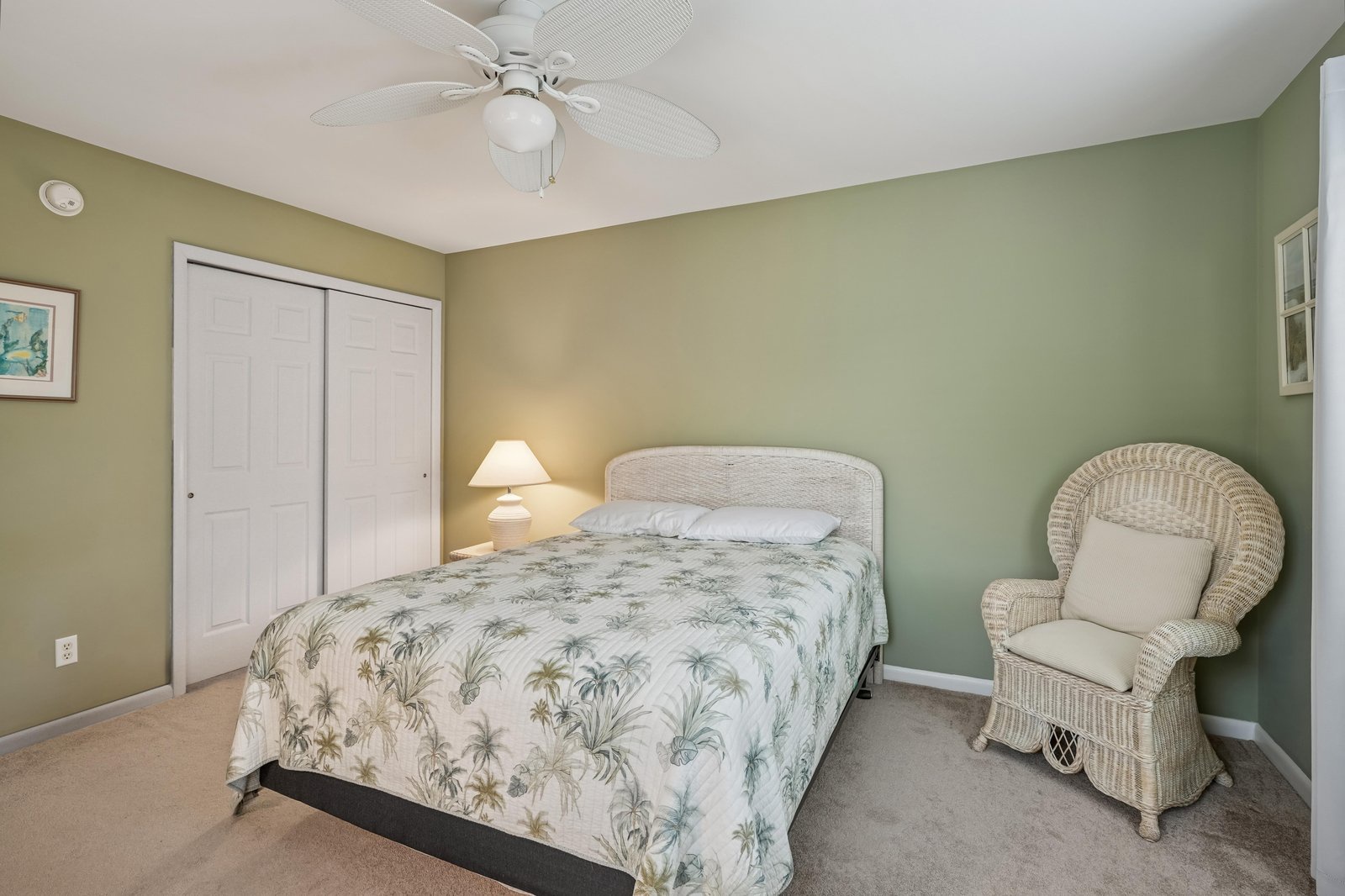 Drift off in your serene retreat, featuring a cozy bed dressed in tropical linens, a gentle ceiling fan for comfort, and a wicker chair to curl up with your favorite book.