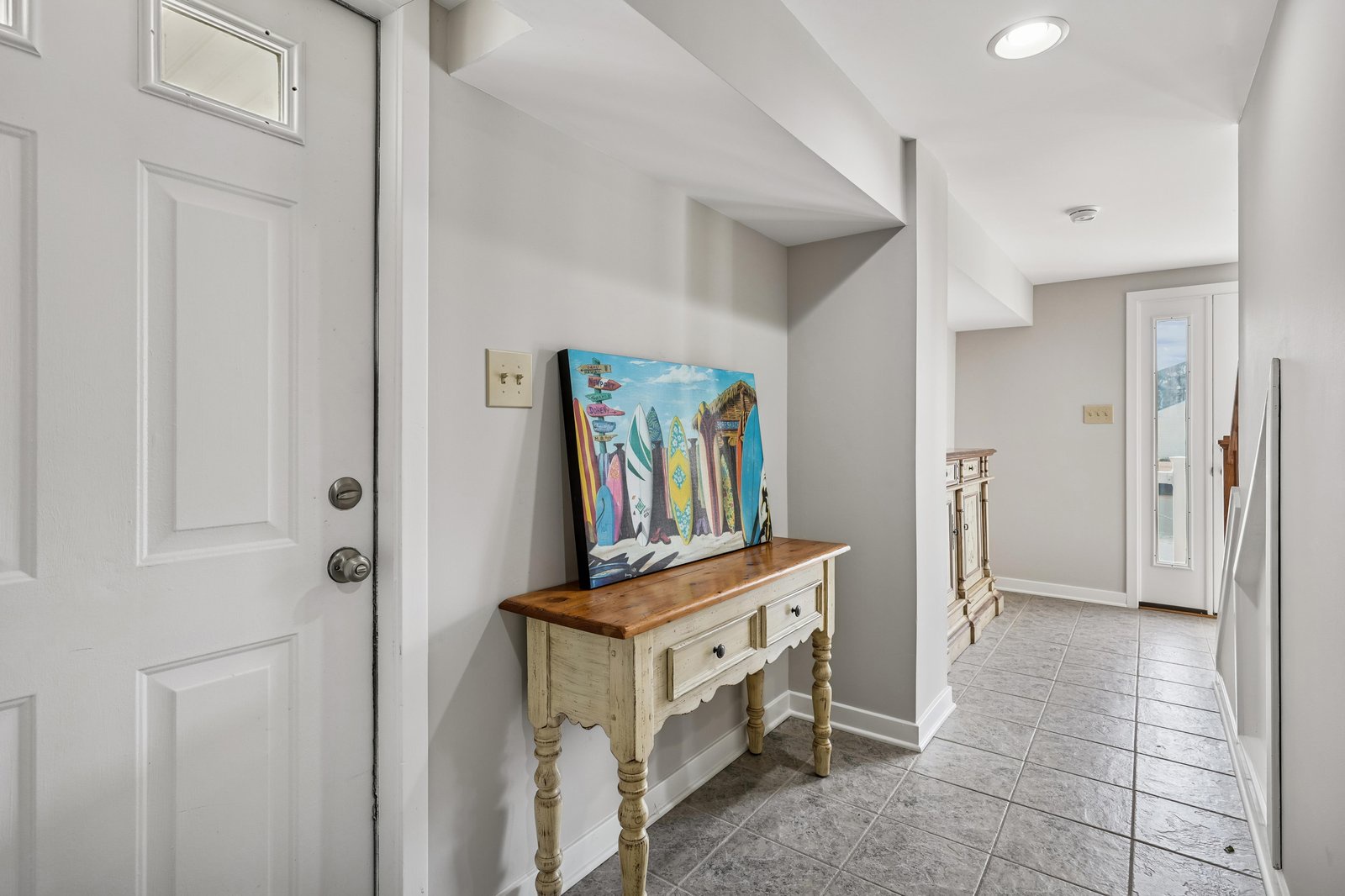 Light-filled entryway welcomes you with coastal charm and thoughtful details, including tile floors, vintage-inspired furniture, and playful beach-themed artwork that sets a relaxed vacation tone.
