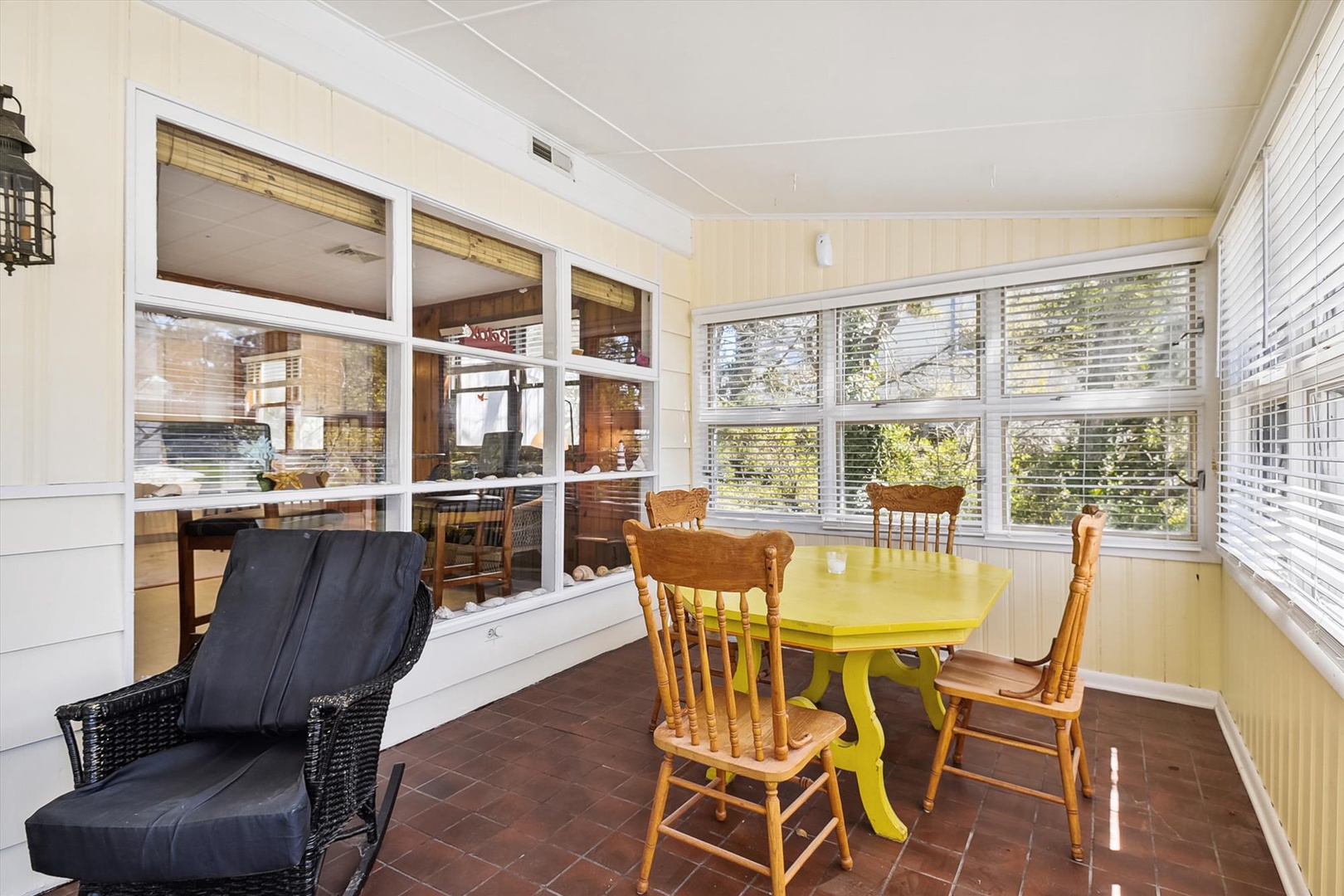 Your cozy sunroom retreat features a cheerful yellow dining table with classic wooden chairs, perfect for morning coffee or casual meals while enjoying garden views through bright windows.
