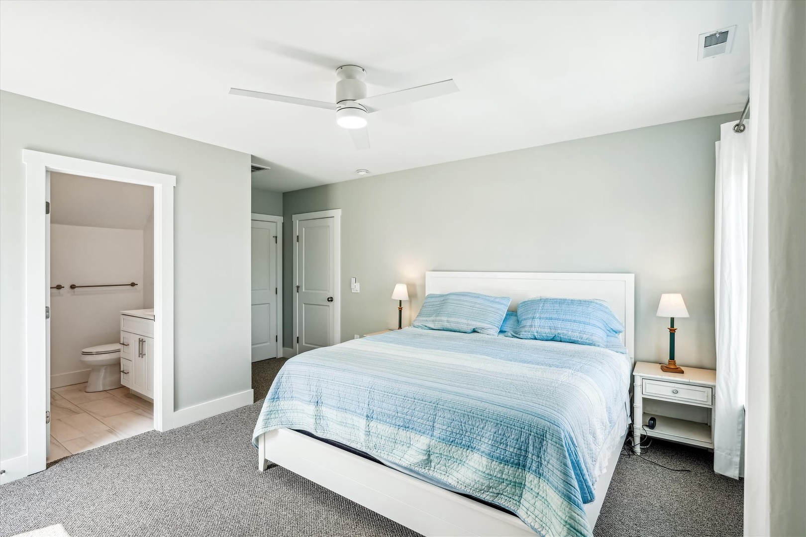 Relax in your peaceful bedroom featuring soothing blue linens, bedside lamps, and an ensuite bathroom for your convenience.