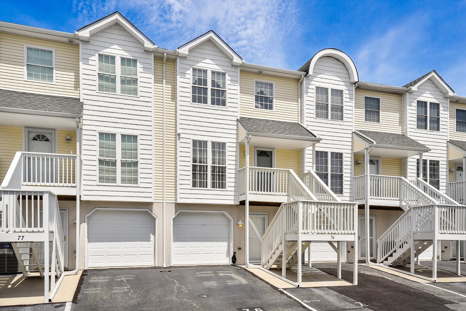 A row of modern townhomes featuring elevated entrances, private parking spaces, and bright coastal-style architecture under a clear blue sky.