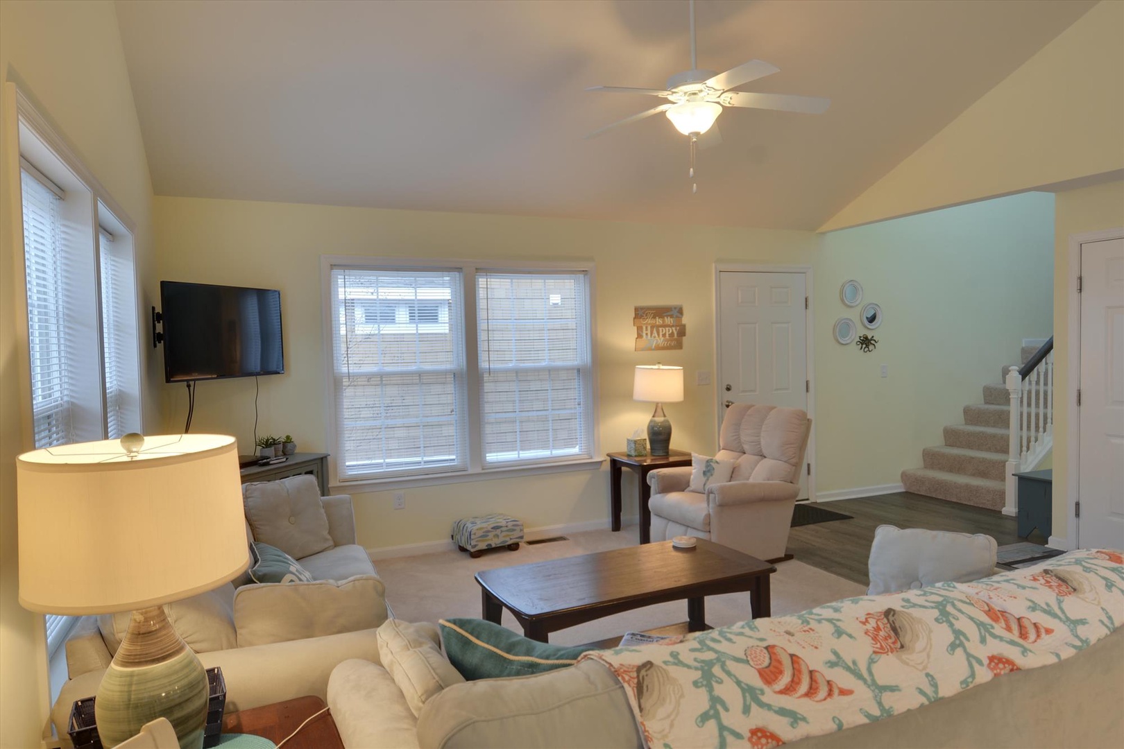 Unwind in your inviting living room featuring plush seating, a wall-mounted TV, and soft natural light streaming through multiple windows—your perfect space to relax and gather.