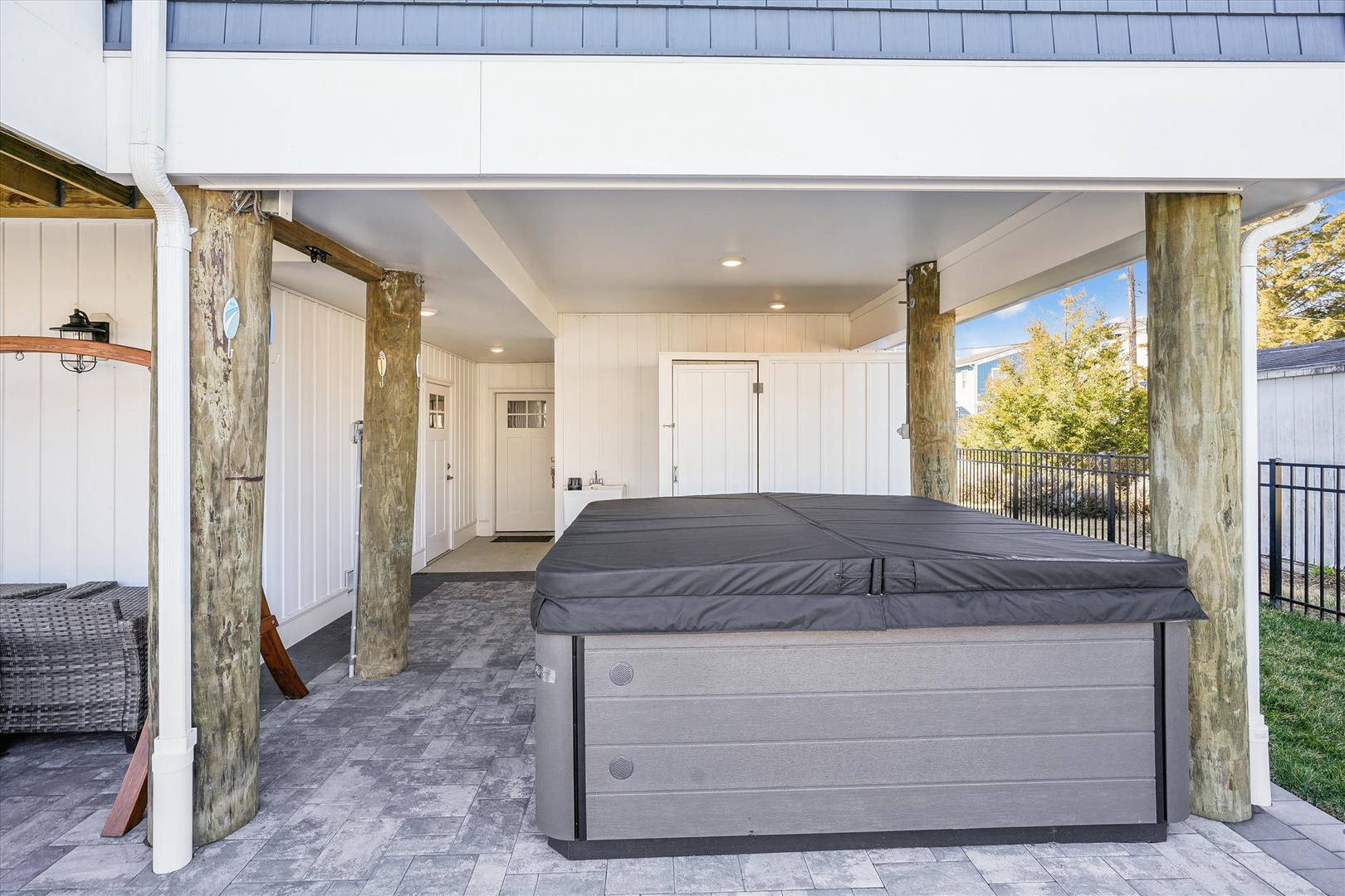 A covered patio area features rustic timber posts and ample space with a hot tub, outdoor seating, and easy backyard access—ideal for relaxing after exploring the area.