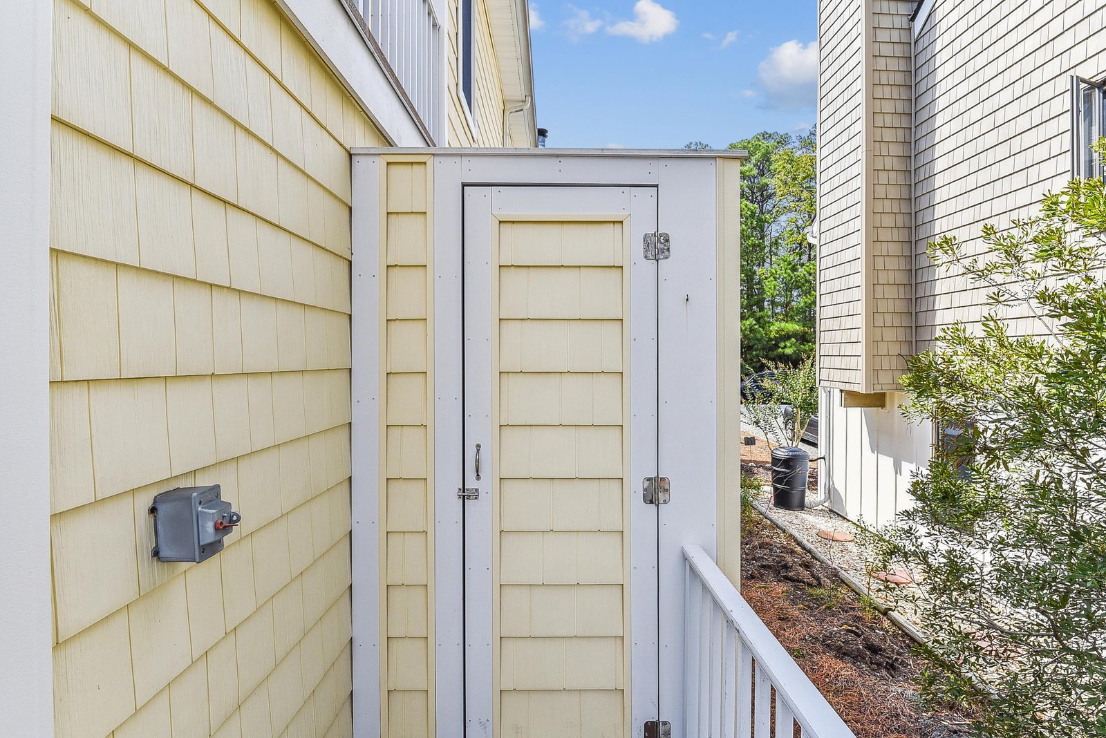 The side entrance leads through a quiet outdoor corridor bordered by mature greenery, connecting the buildings to nearby amenities and offering a peaceful arrival experience.