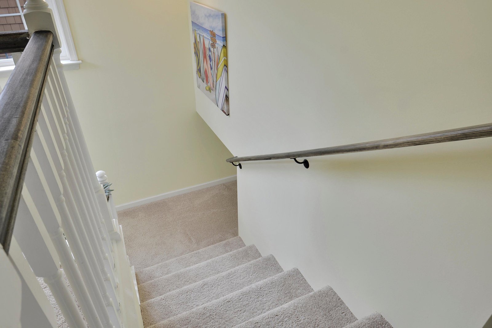 Freshly carpeted stairs with sturdy handrails connect your floor levels, brightened by natural light and thoughtful touches like cheerful wall art.