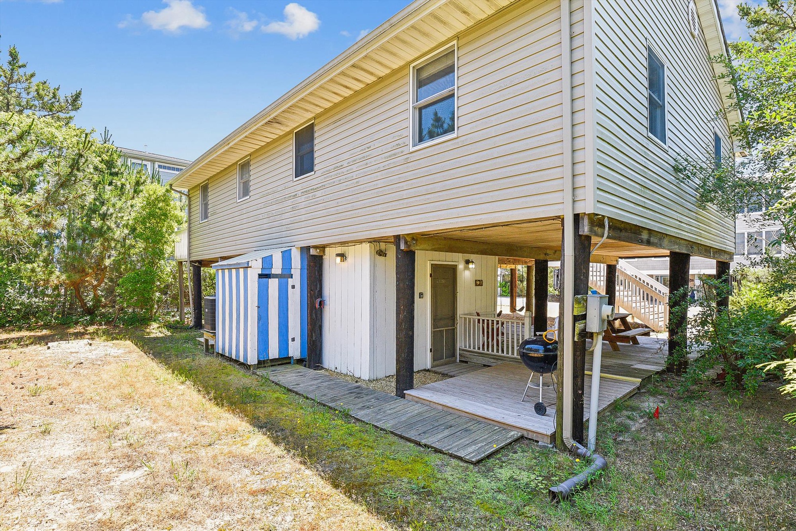 This beach rental features a two-story structure with covered outdoor areas, BBQ setup, and convenient storage beneath the main living space.