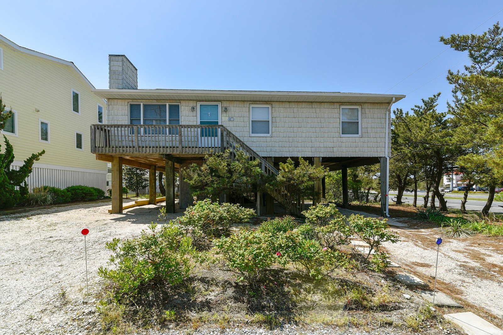 This coastal property sits elevated above ground level among natural landscaping and mature trees, offering a charming exterior and easy access to the surrounding area.