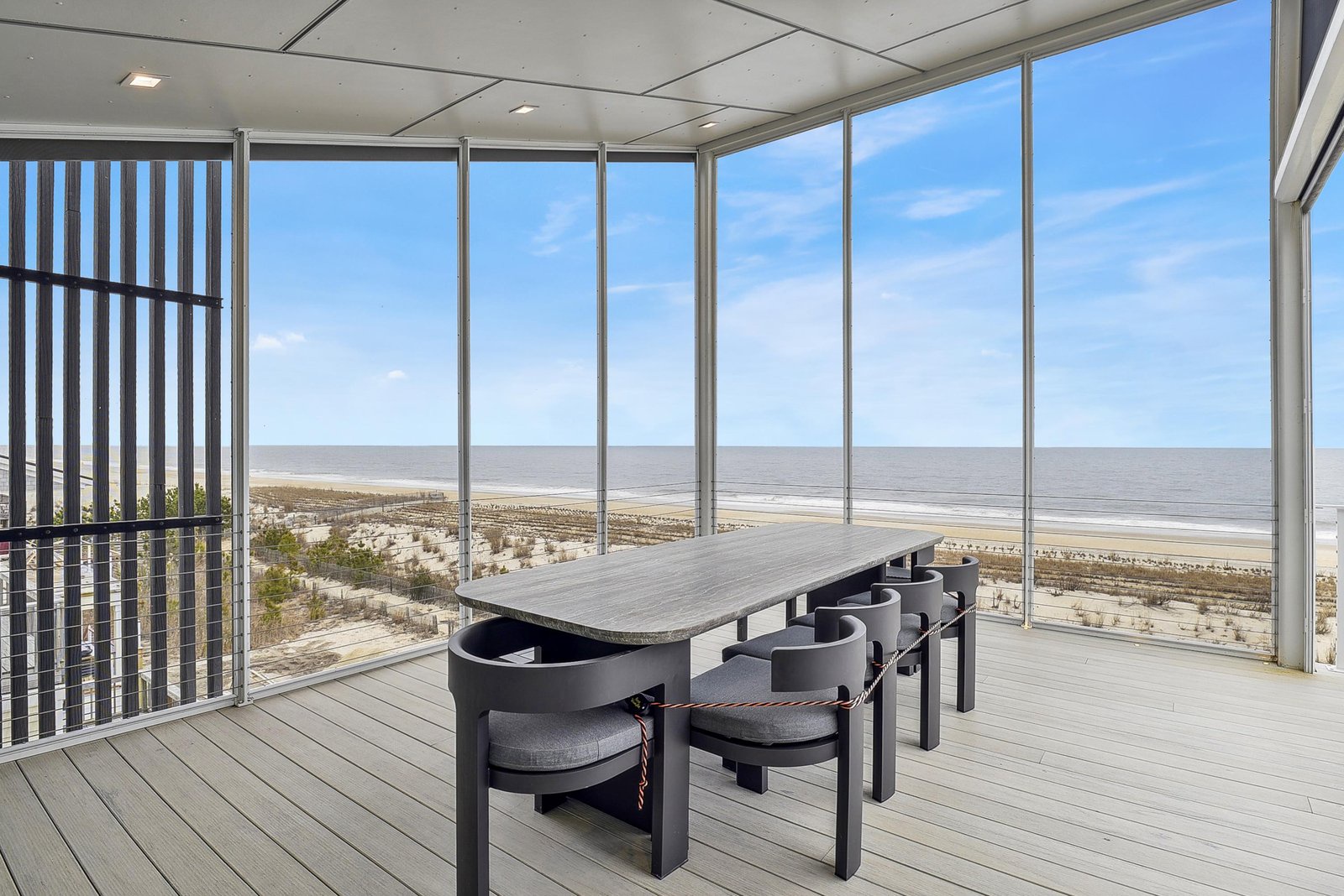 This sunlit terrace offers a stunning beachfront view where sandy shores meet the ocean horizon, creating the perfect backdrop for your morning coffee or evening gatherings at the sleek dining table.