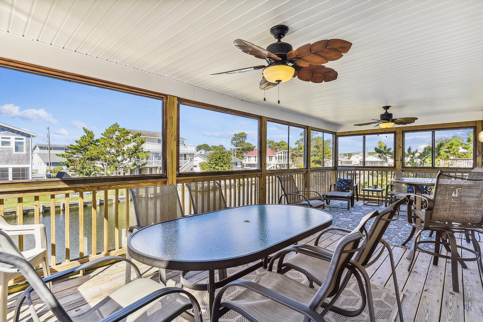 Step into your screened porch where coastal breezes meet comfort—gather around the spacious dining table, relax under ceiling fans with tropical flair, and soak in neighborhood views through panoramic windows.