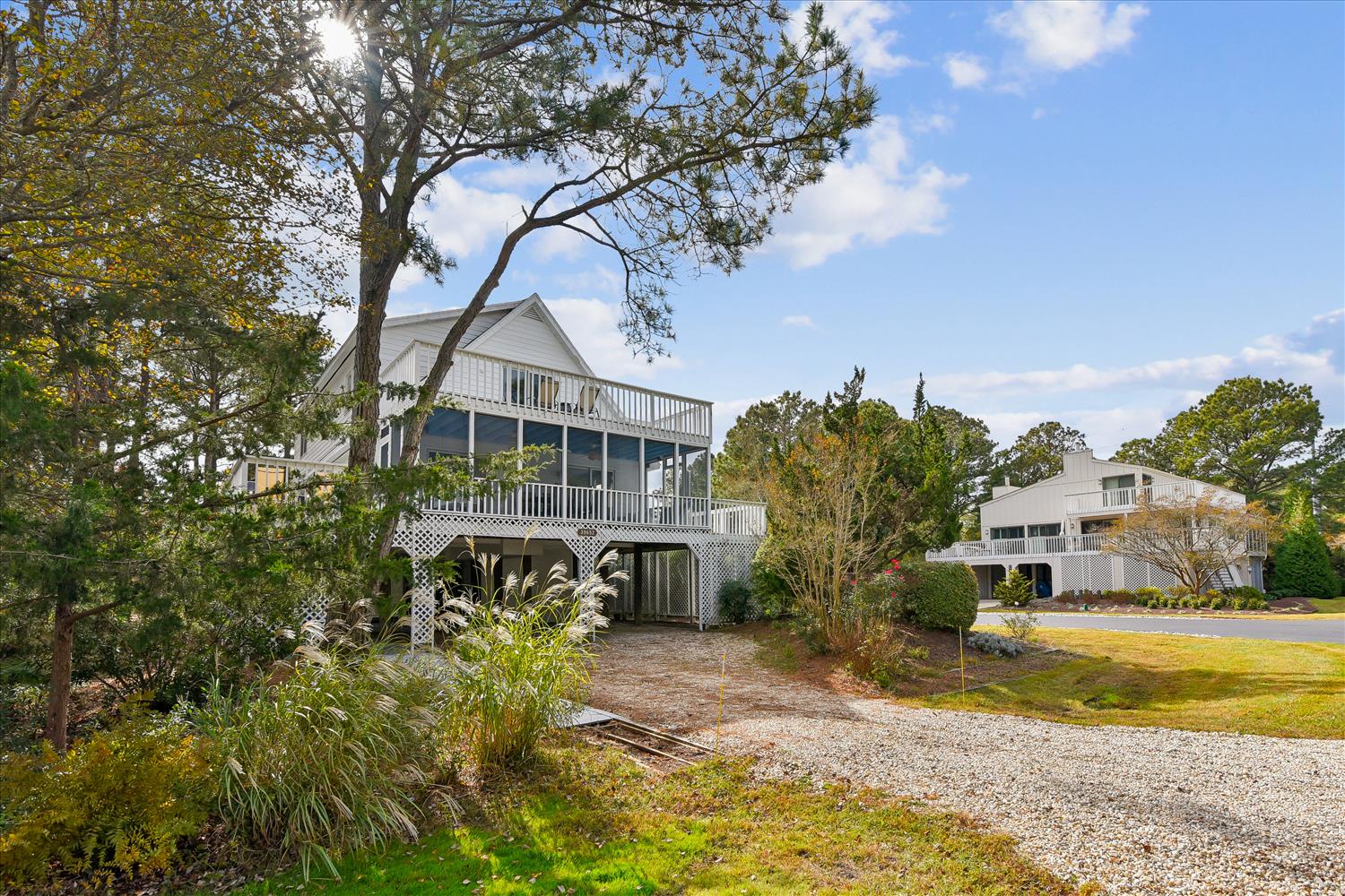 Charming elevated beach house nestled among mature trees with spacious decks and coastal architecture in a peaceful neighborhood setting.