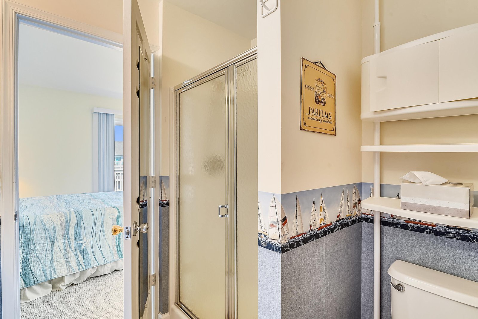 Your private bathroom features a spacious glass-enclosed shower, with charming coastal touches like model sailboats adding a nautical feel.