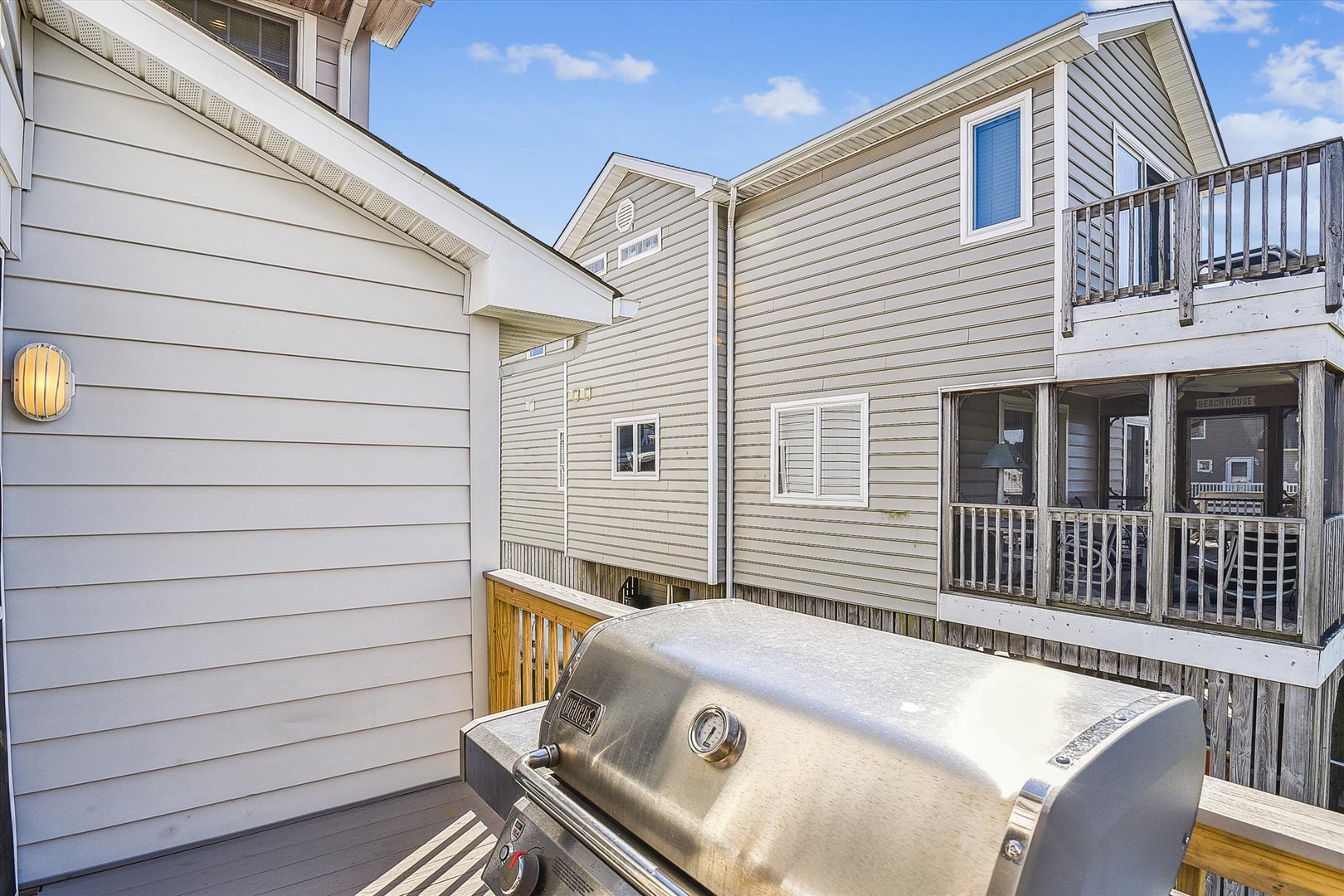 Private deck with stainless steel grill positioned between neighboring properties under clear skies, ideal for outdoor cooking during your stay.