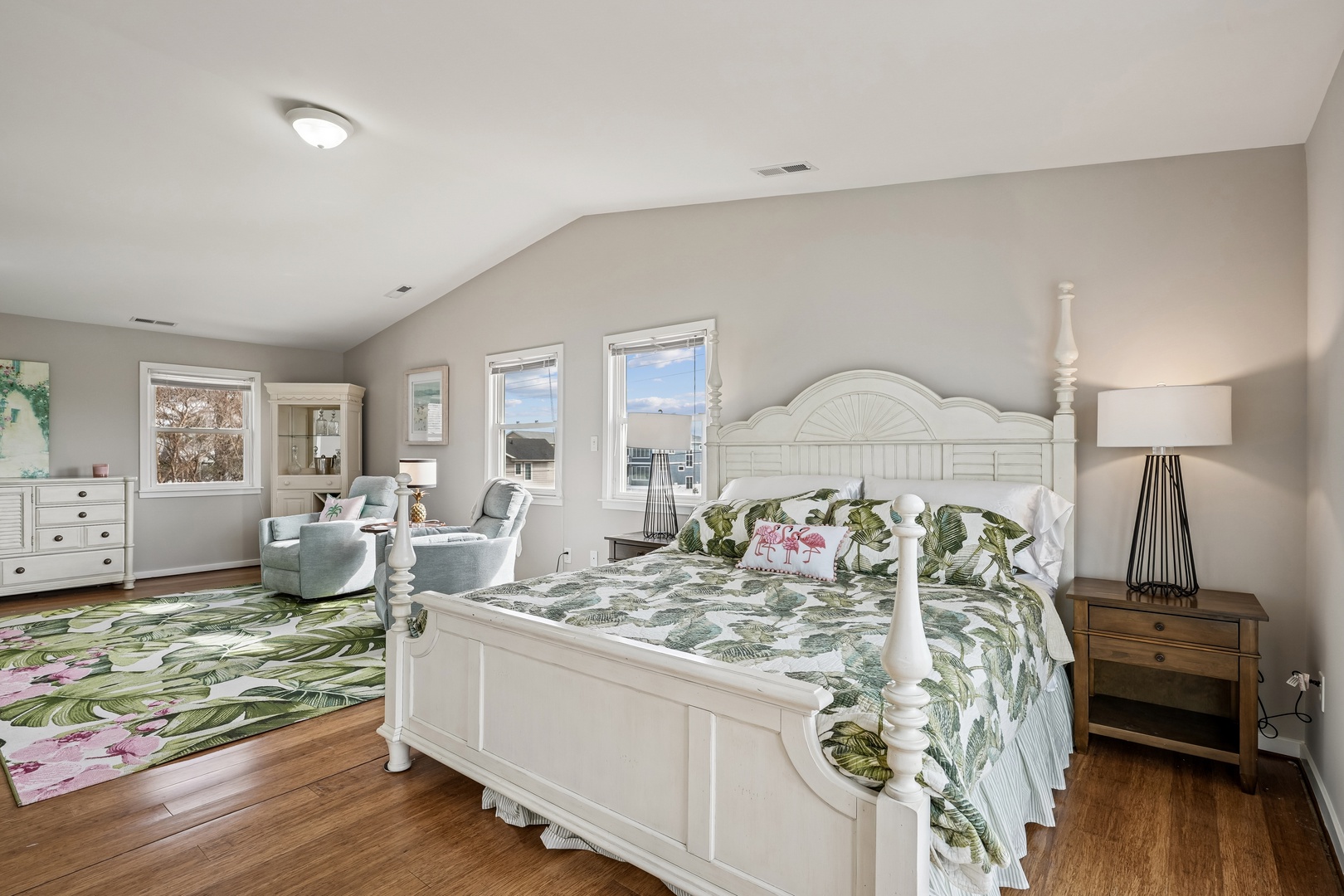 Sink into tropical comfort with botanical bedding and cozy seating where natural light streams through windows.