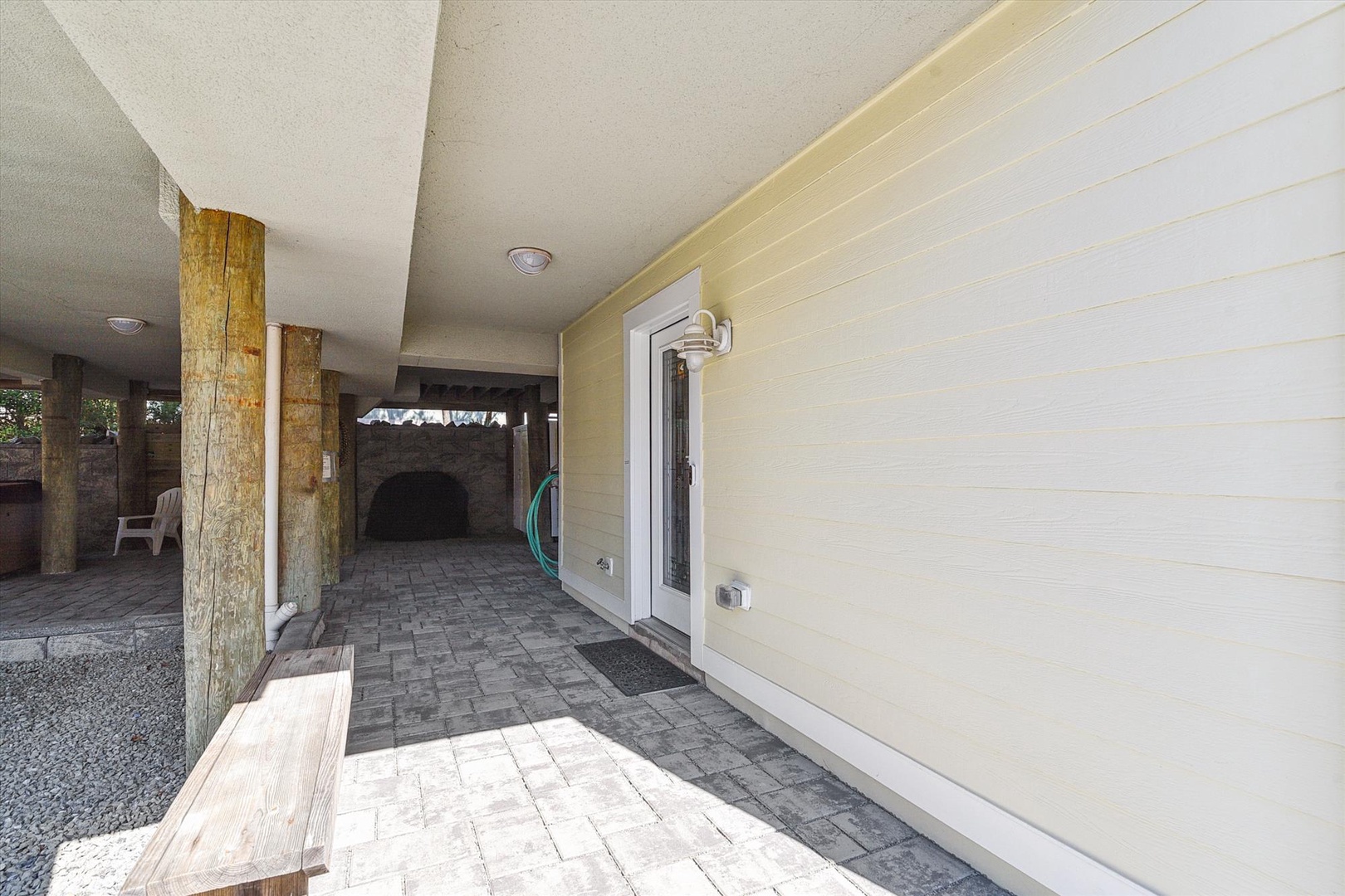 Covered outdoor entry area with rustic wood posts, paver flooring, and a built-in fireplace for gathering on cooler evenings.