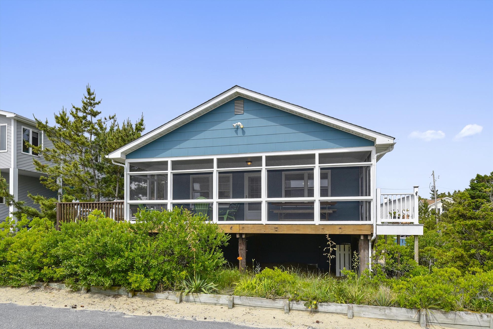 A charming beach cottage with screened porch, nestled among coastal greenery with neighboring homes nearby—a peaceful seaside getaway awaiting your arrival.